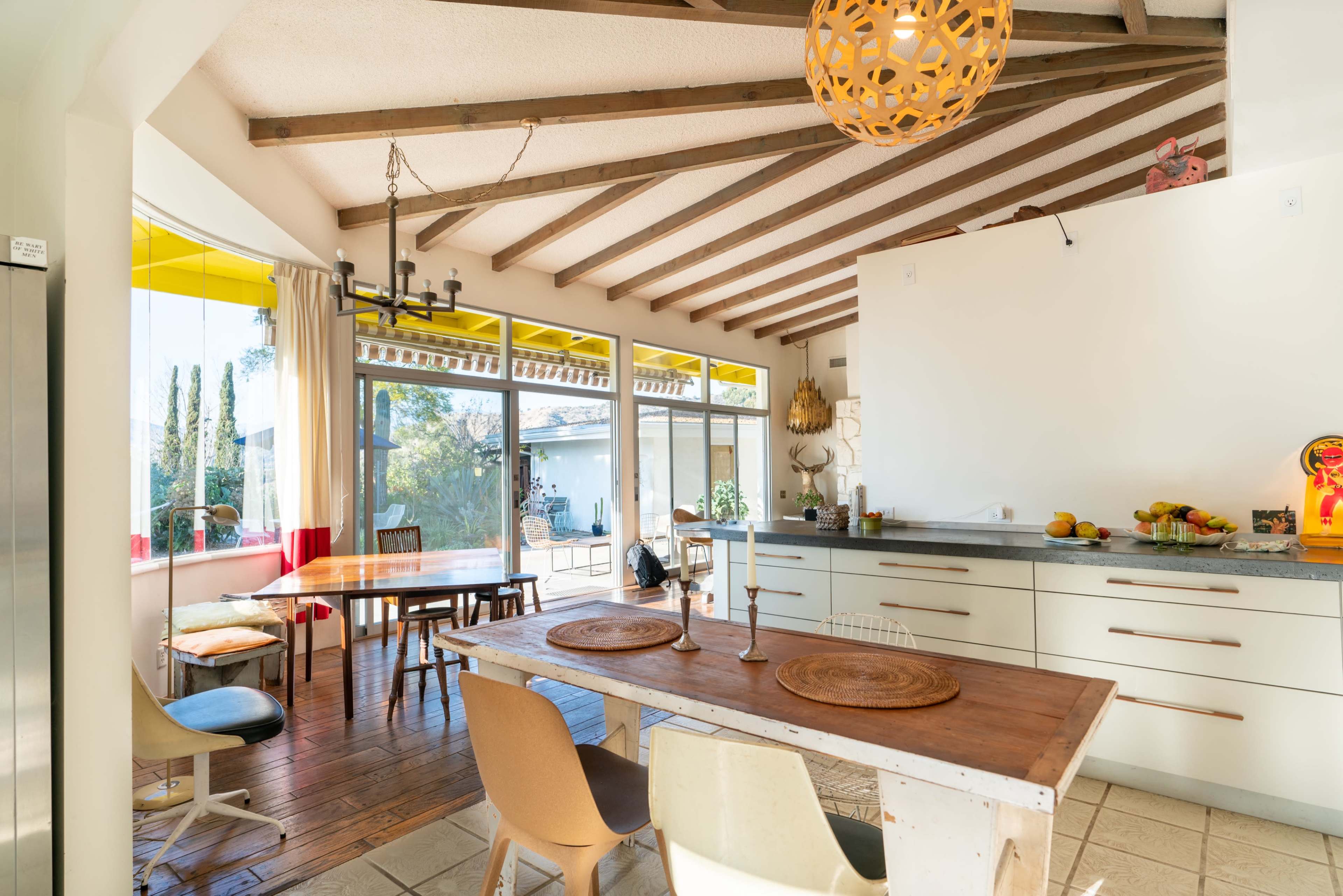 A modern kitchen and dining area with wooden beams, a large window, and a table set with fruits and placemats.