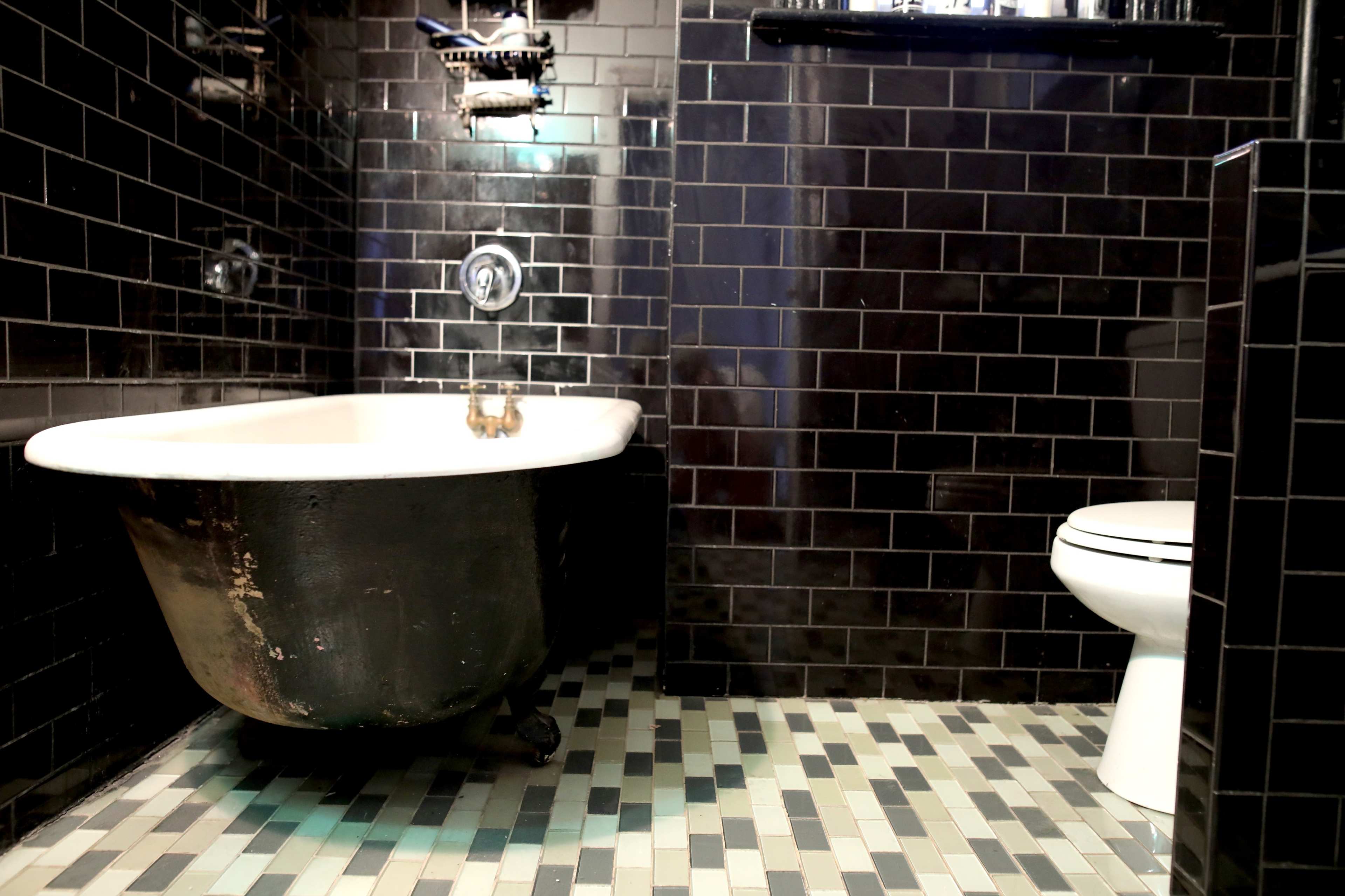 A bathroom featuring a vintage clawfoot bathtub and a modern toilet, with black tiled walls and a mosaic tile floor.