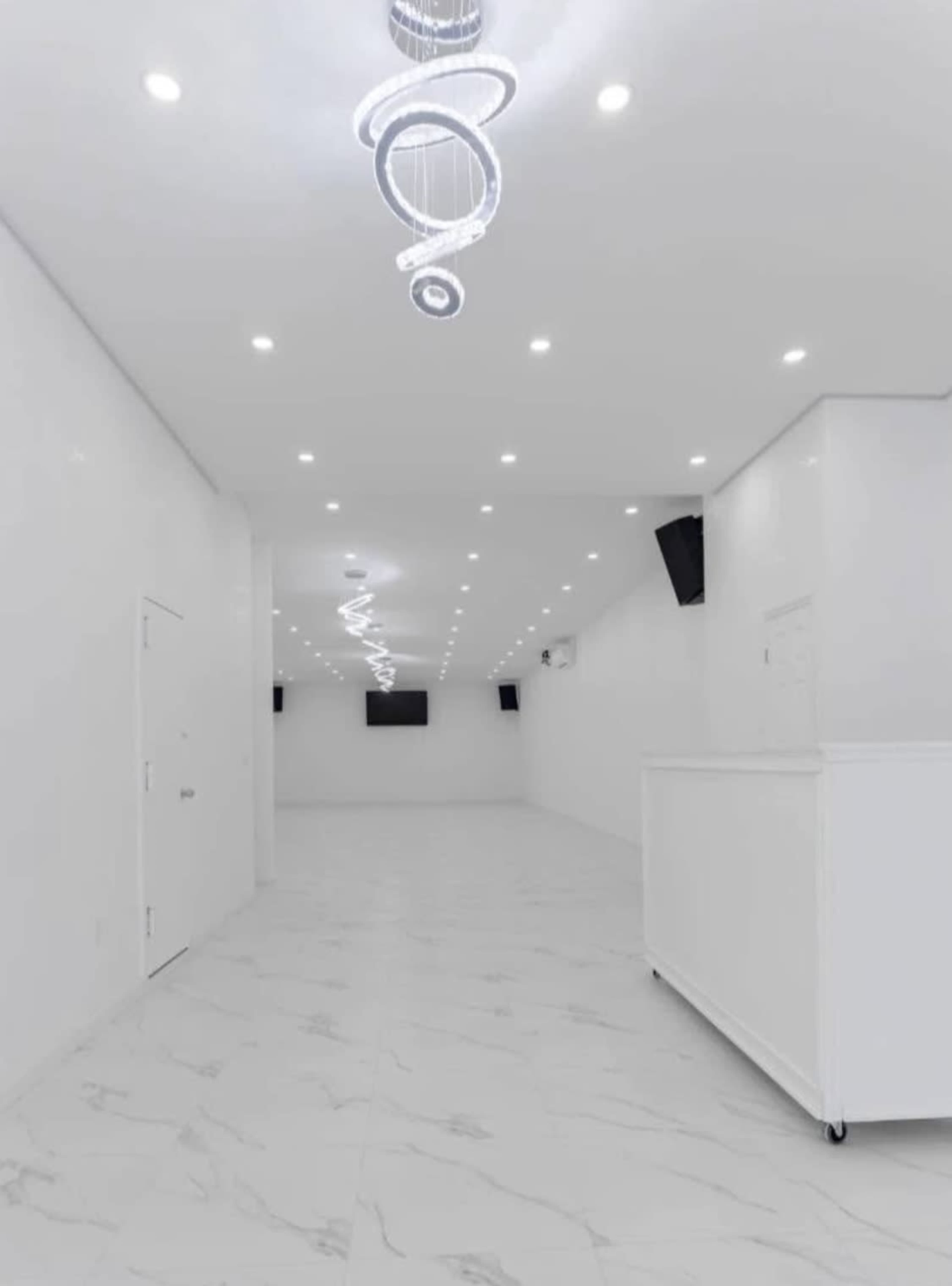 The image shows a spacious and modern interior with a glossy white floor, white walls, and decorative lighting fixtures hanging from the ceiling.