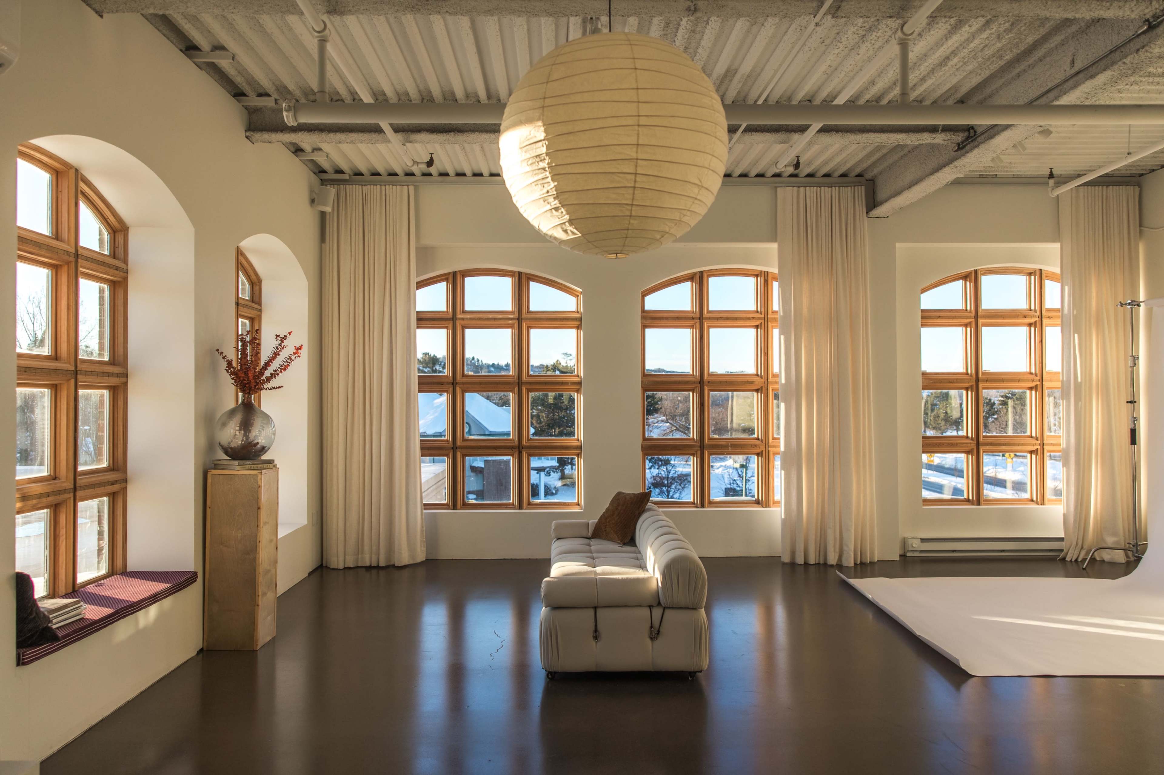 The image shows a modern, airy living room with large arched windows, a light-colored sofa, and decorative elements.