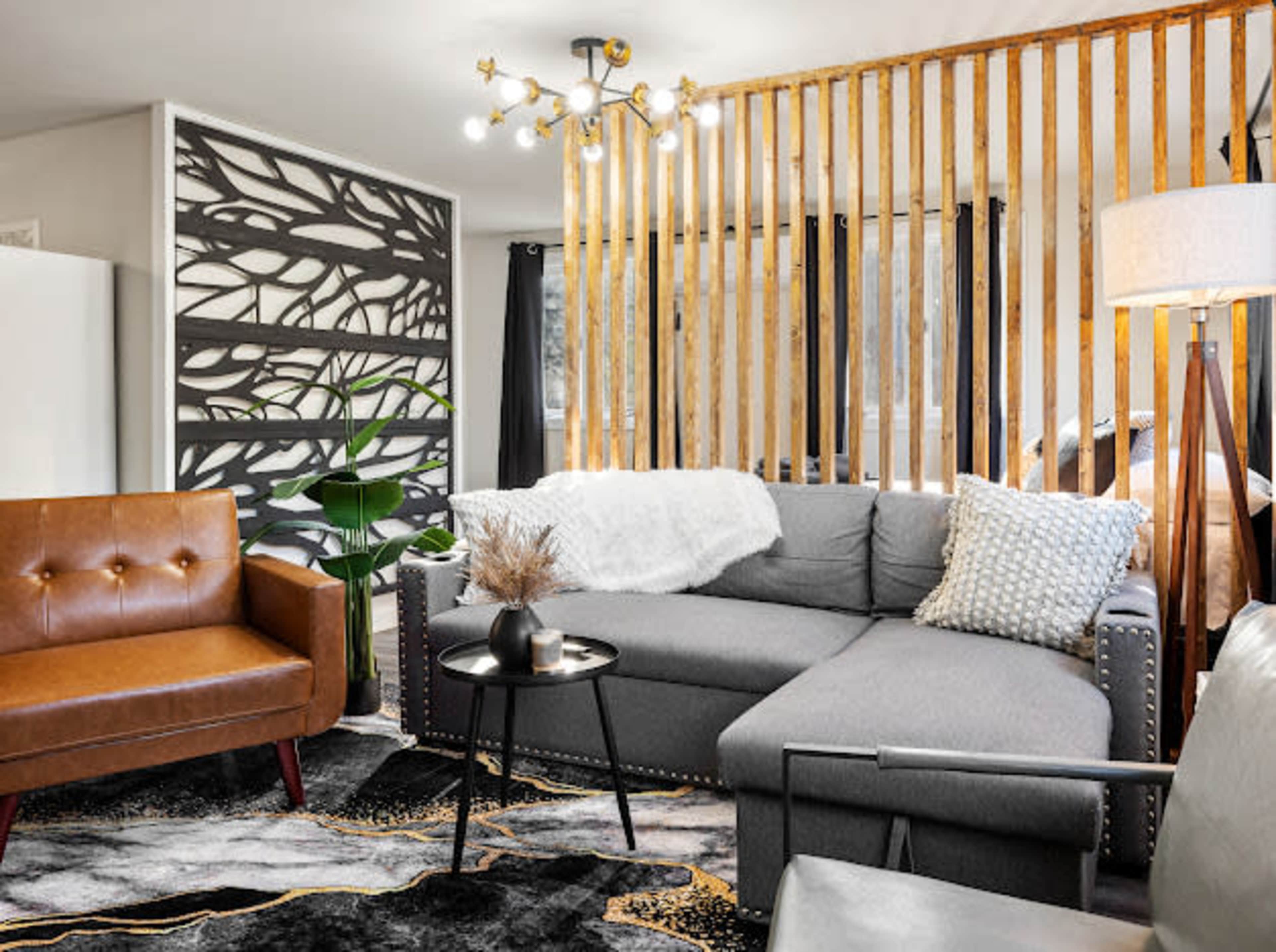 A modern living room featuring a sectional gray sofa, a brown leather accent chair, a decorative light fixture, and a textured area rug.