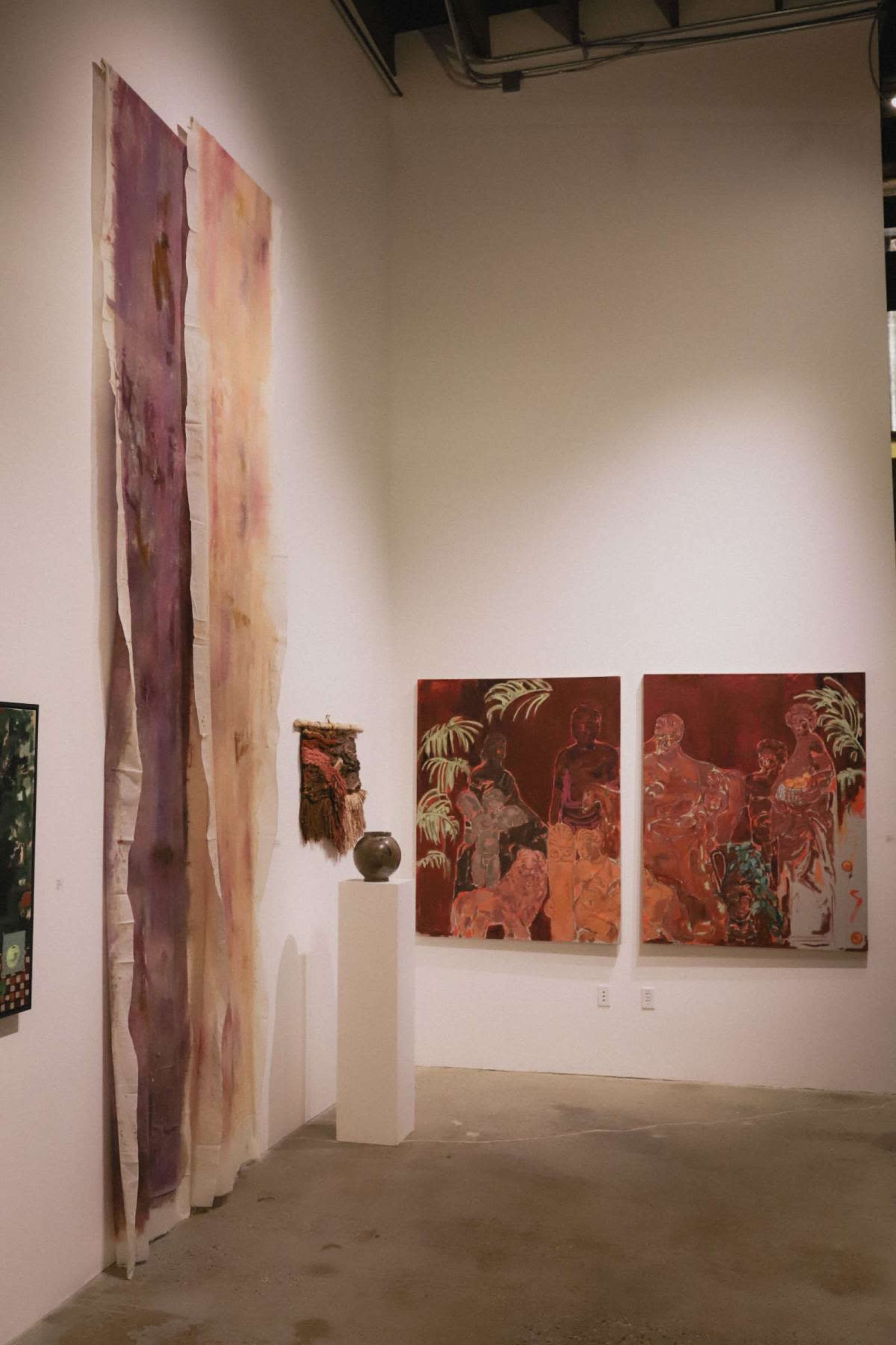 The image shows an art gallery featuring large wall hangings and colorful paintings displayed on a white wall.