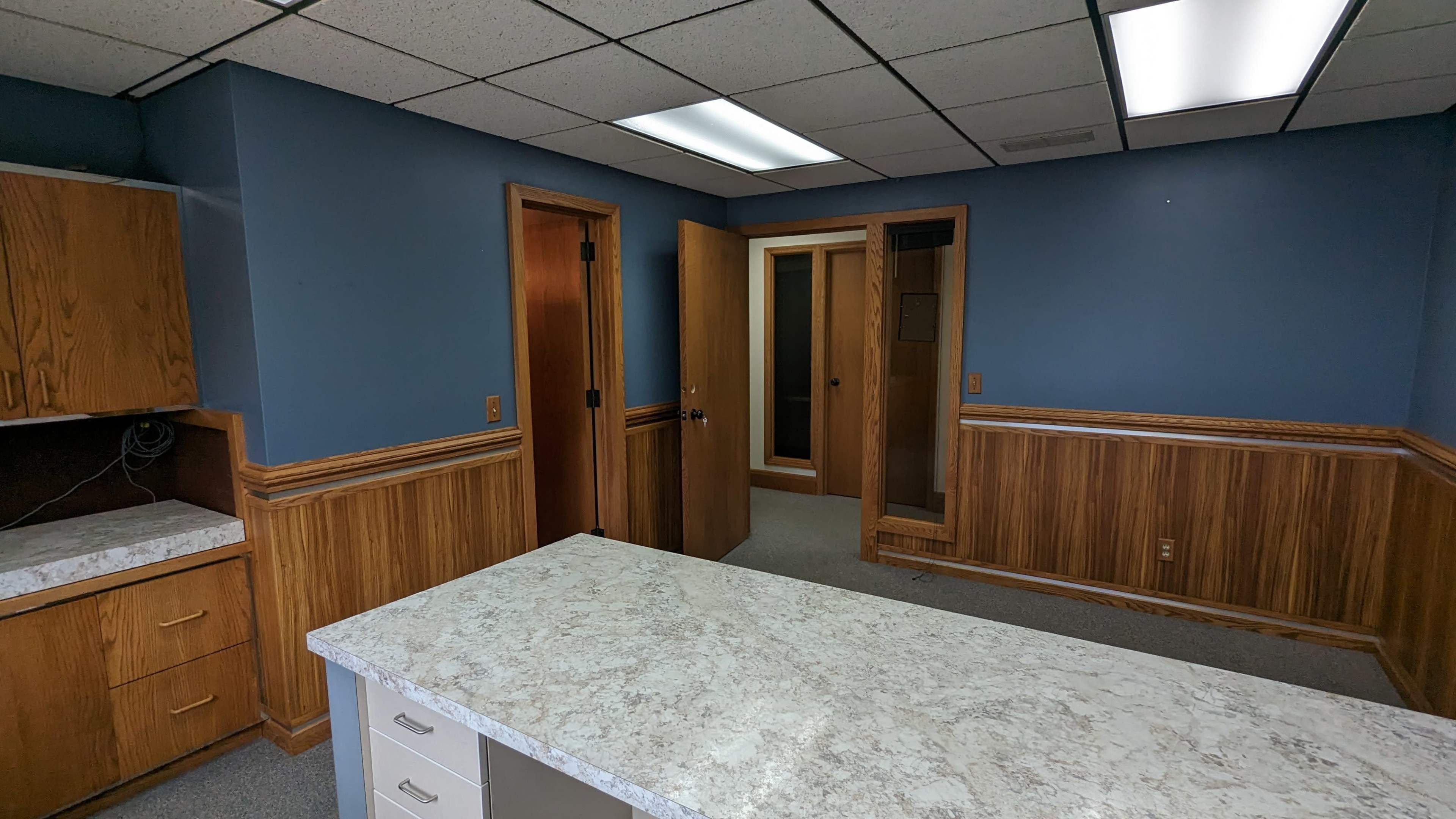 An office space with blue walls, wood paneling, a countertop, and an open door leading to a hallway.