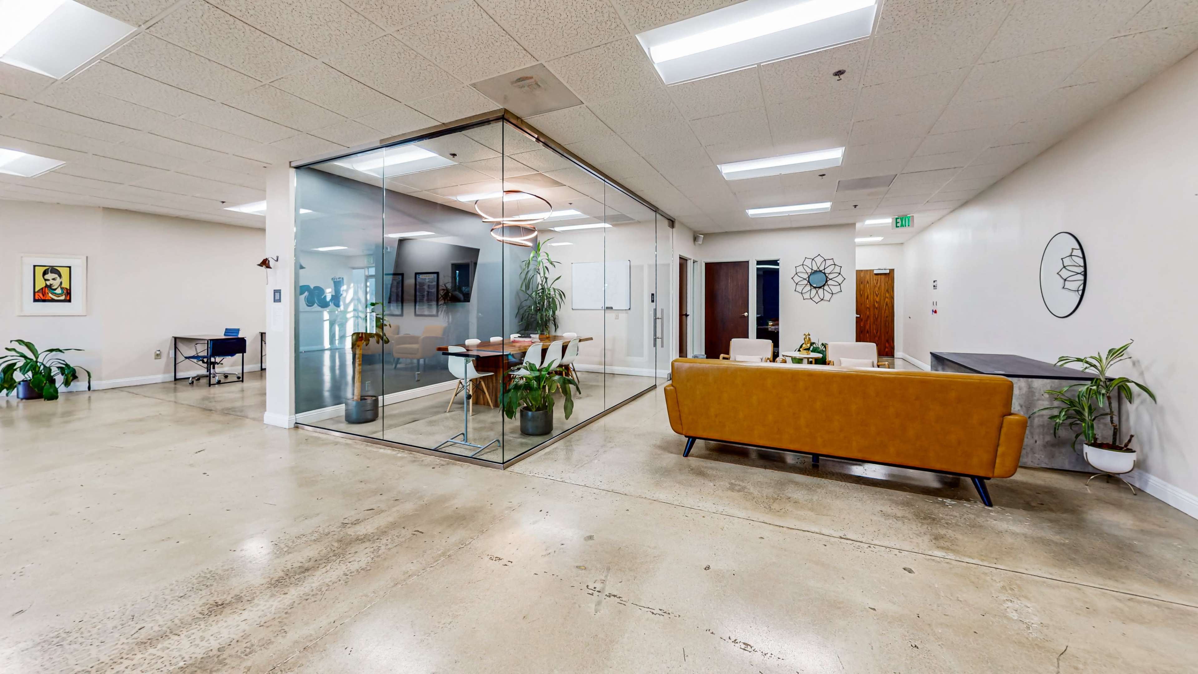 The image shows a modern office space with a glass meeting room, a brown sofa, and plants, all situated on a polished concrete floor.