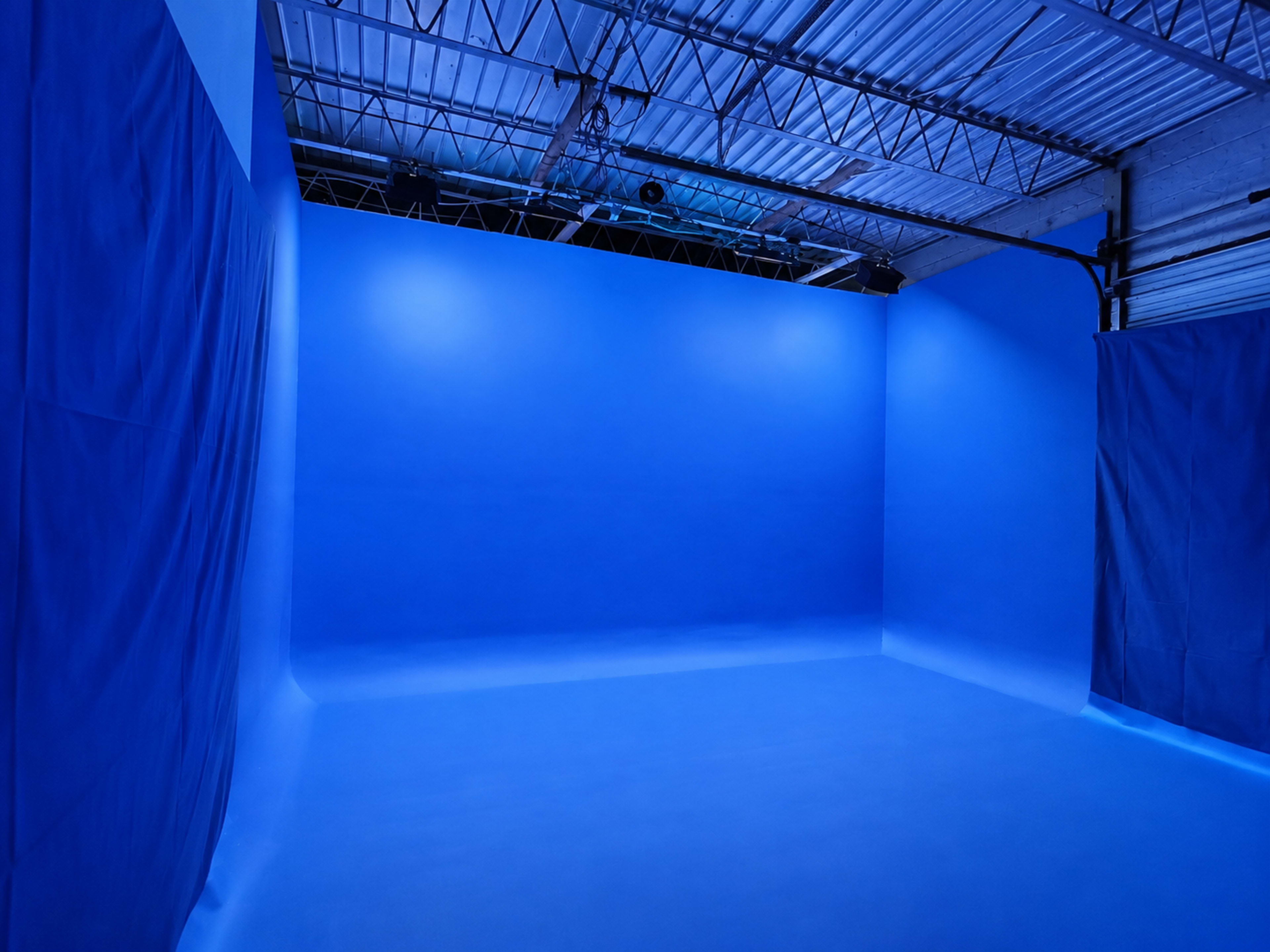 The image shows a large, empty studio space with blue walls and flooring, illuminated by overhead lights.