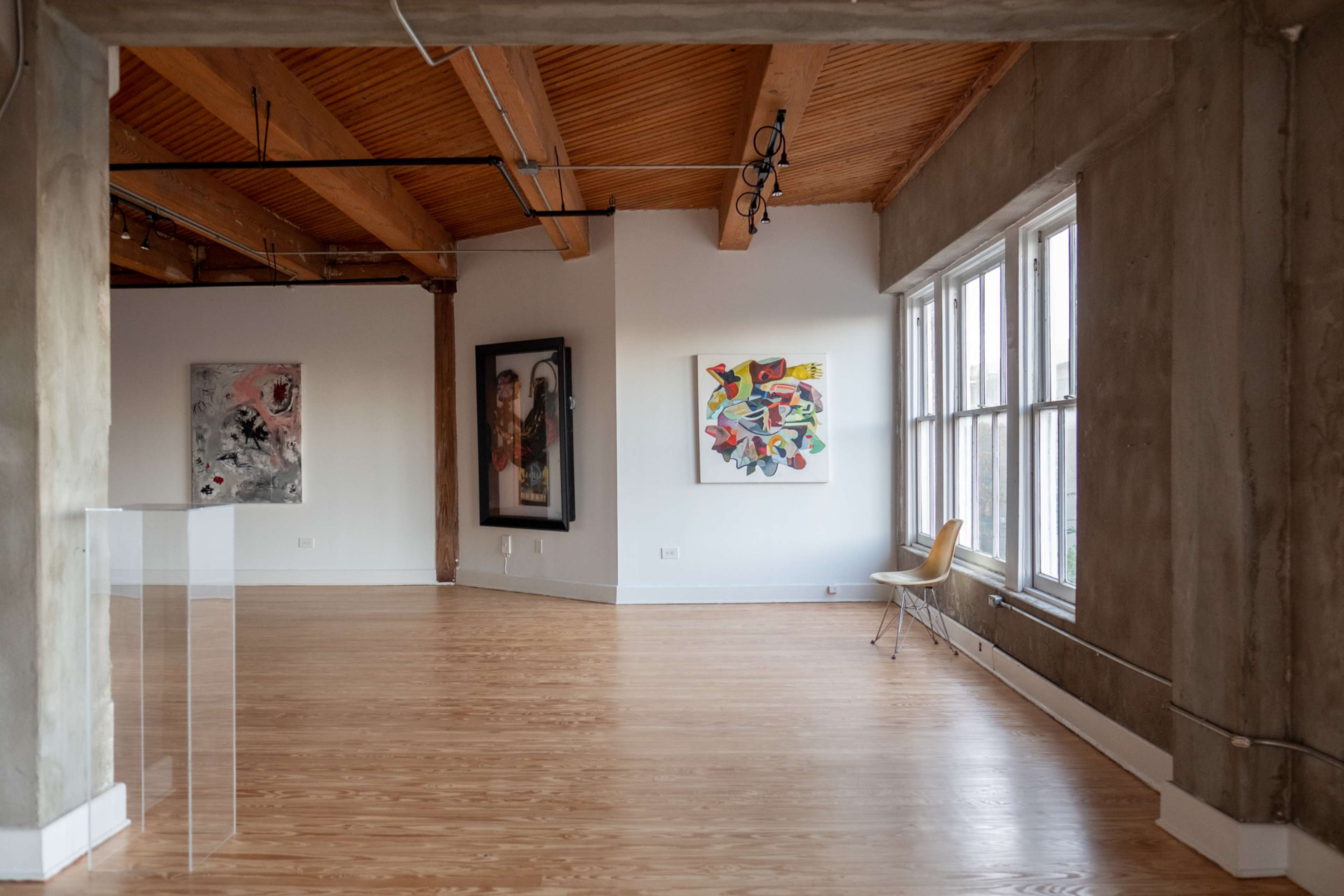 An art gallery features wooden beams, concrete walls, and two abstract paintings displayed against a white backdrop.