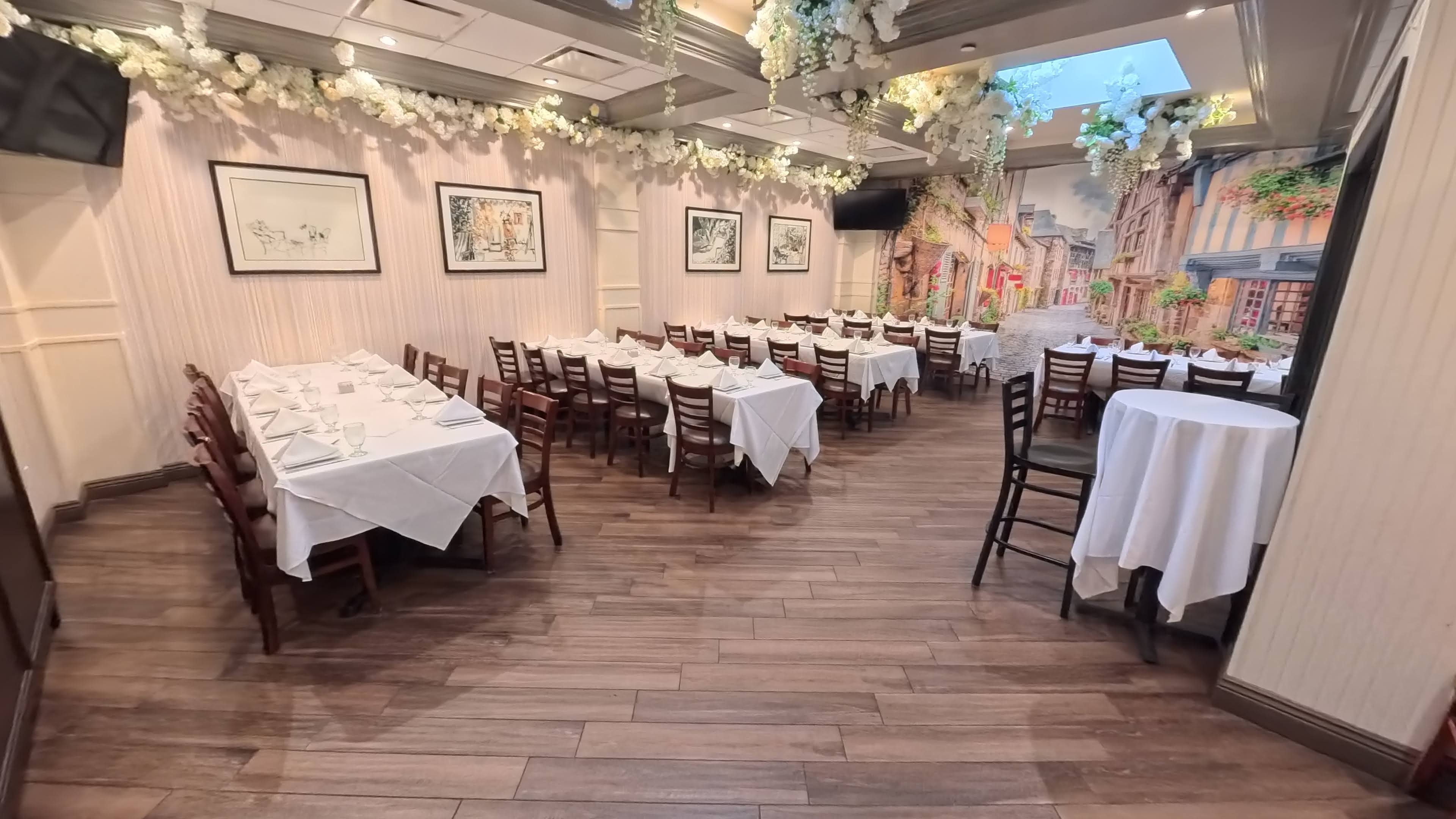 The image shows a restaurant interior with white tablecloths on the tables, wooden chairs, and a wall mural depicting a street scene.