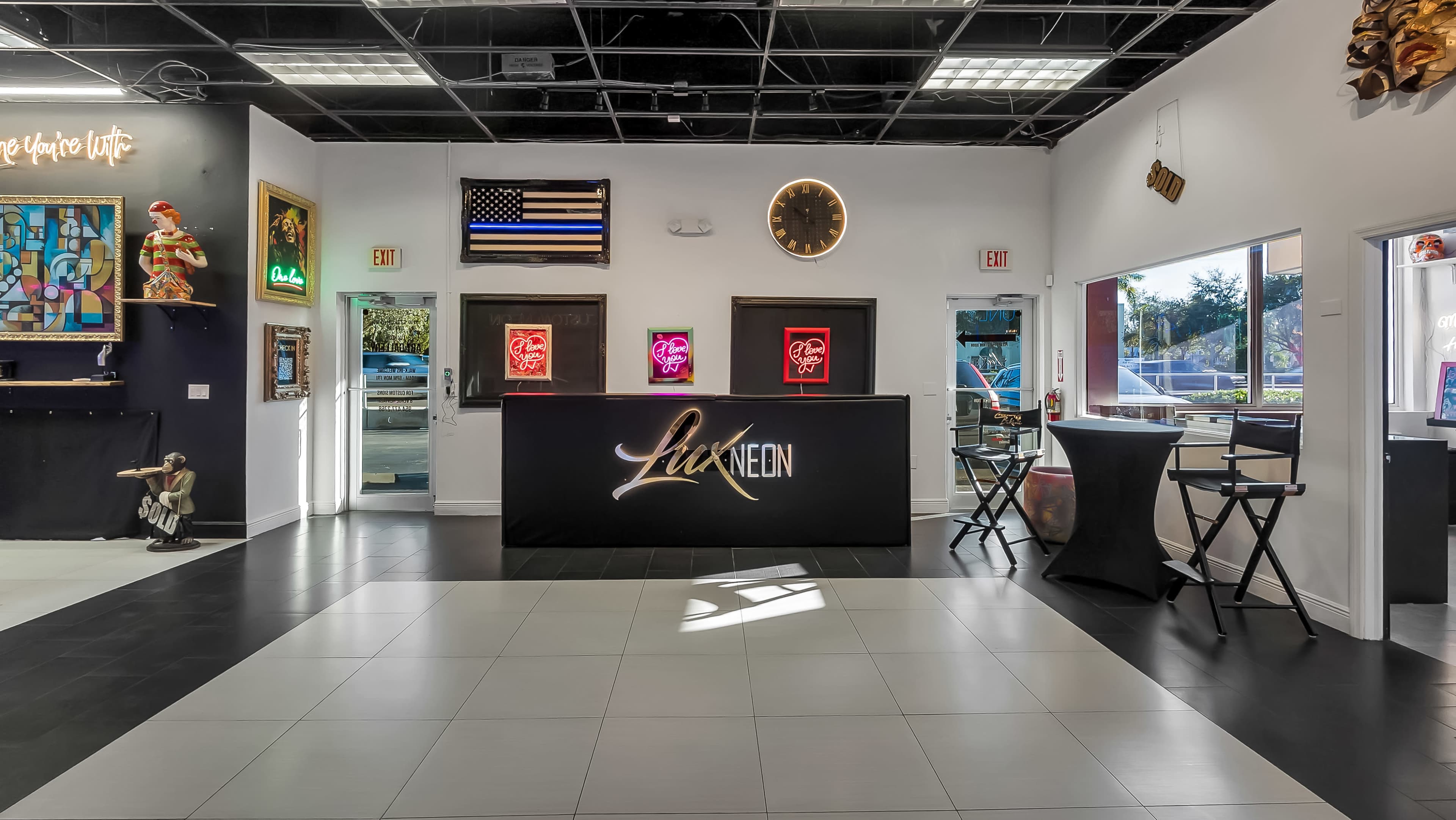 The image depicts a modern reception area with a black front desk featuring the name "Lux Neon," surrounded by colorful neon signs and artwork on the walls.