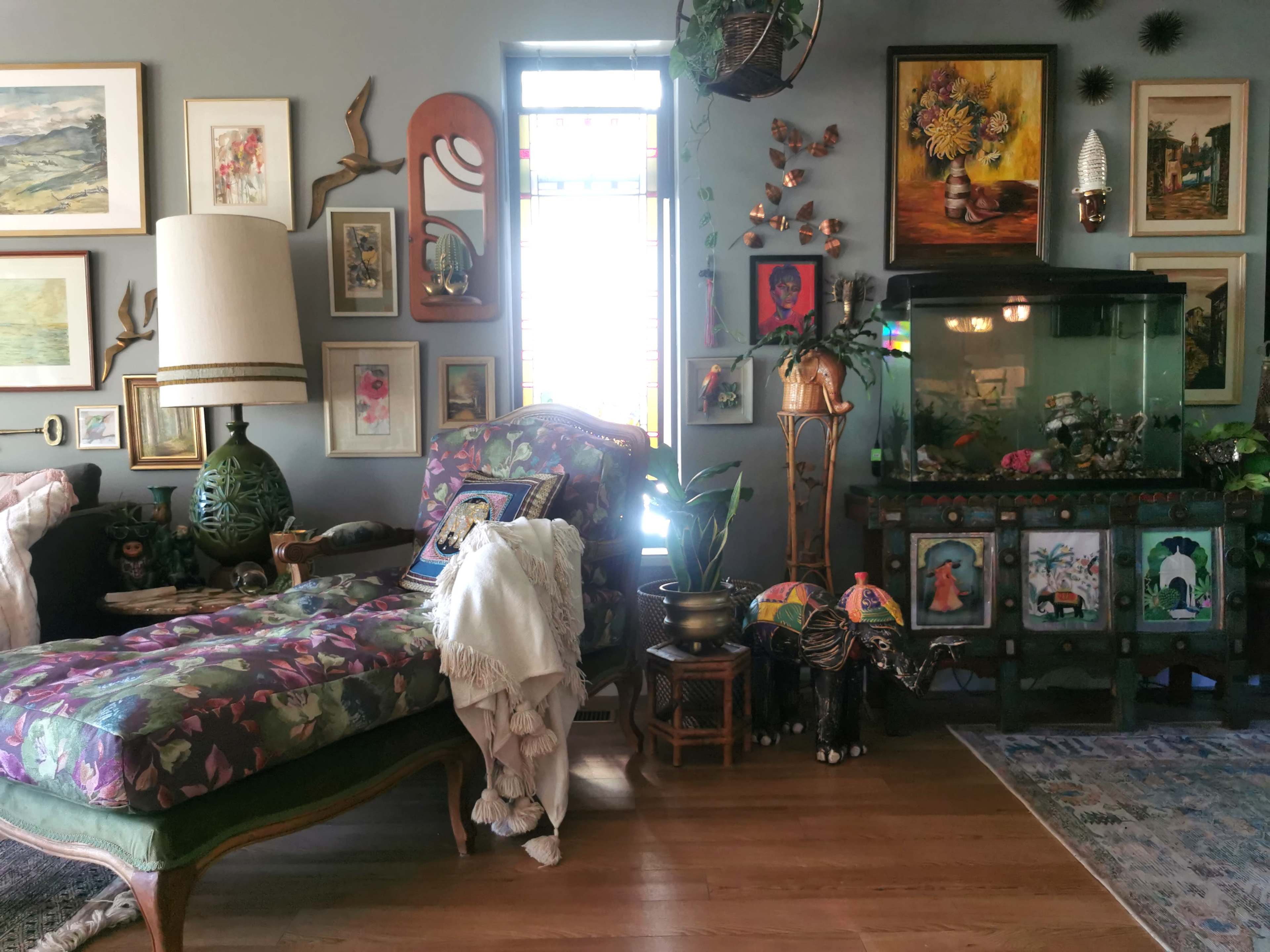 The room features a floral patterned chaise lounge next to a decorated aquarium, surrounded by various framed artworks and decorative items.