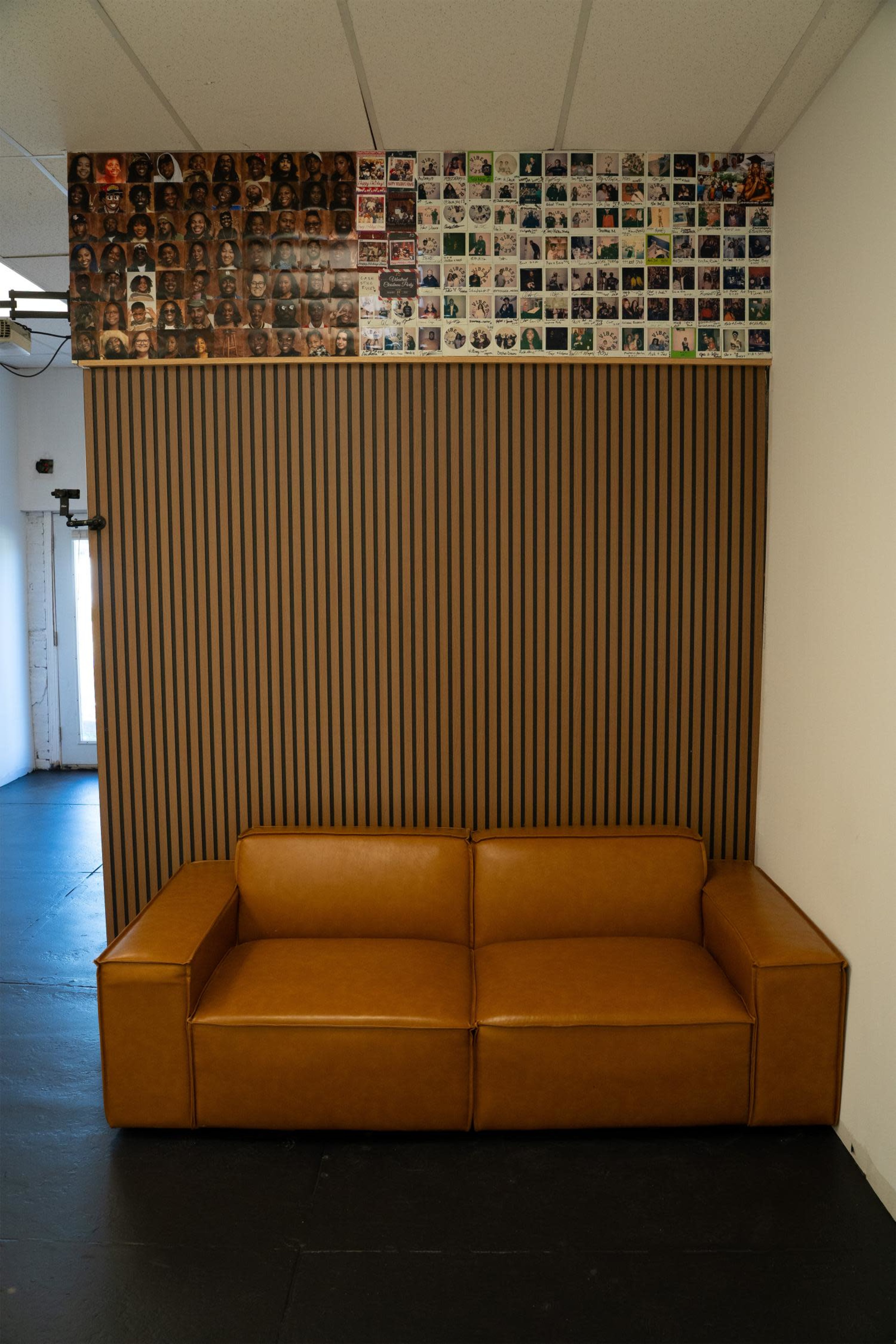 The image shows a brown leather couch against a striped wooden wall, with a collage of photographs mounted above it.