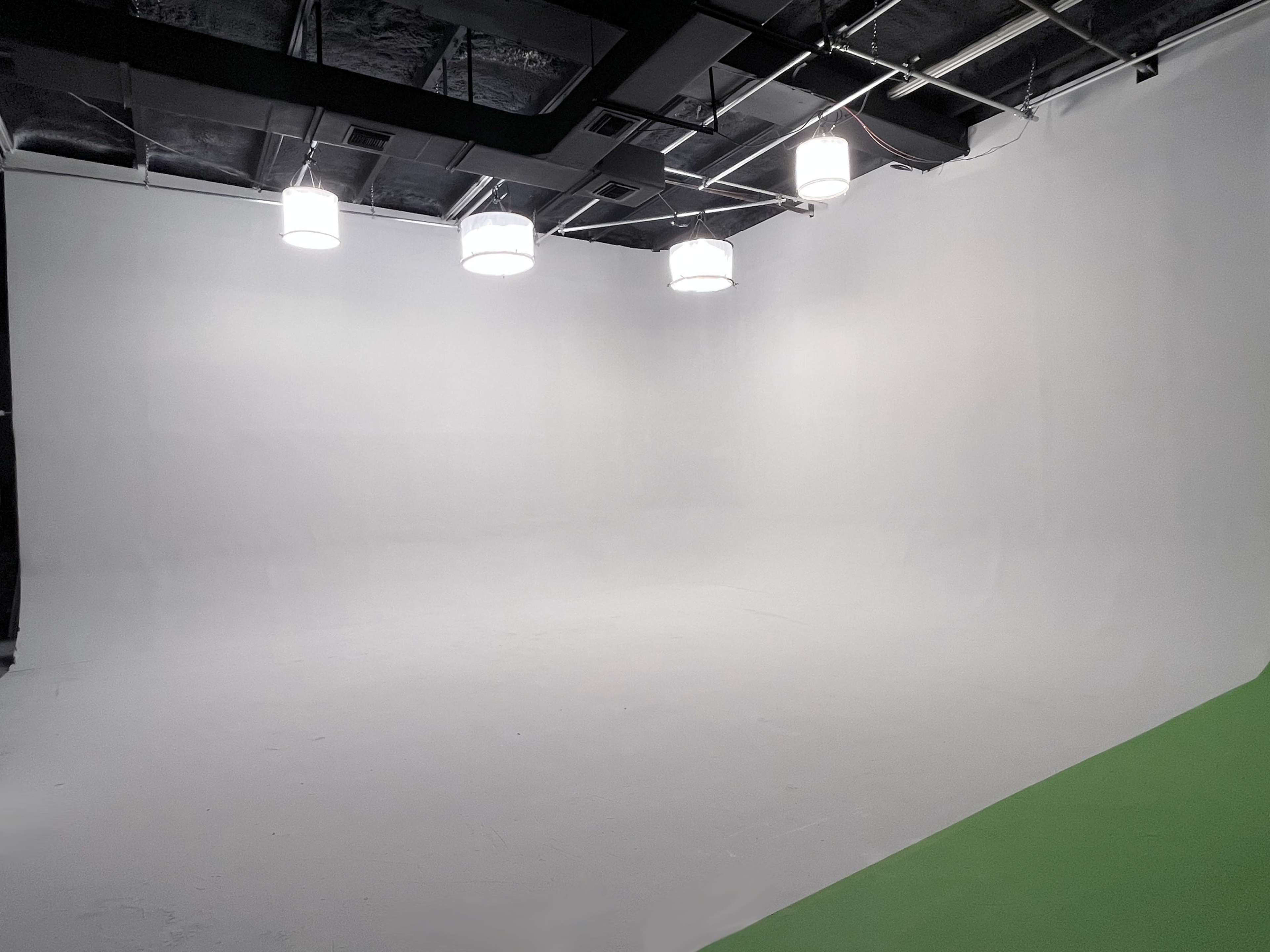 The image shows an empty photo studio with a white seamless background and overhead lights.
