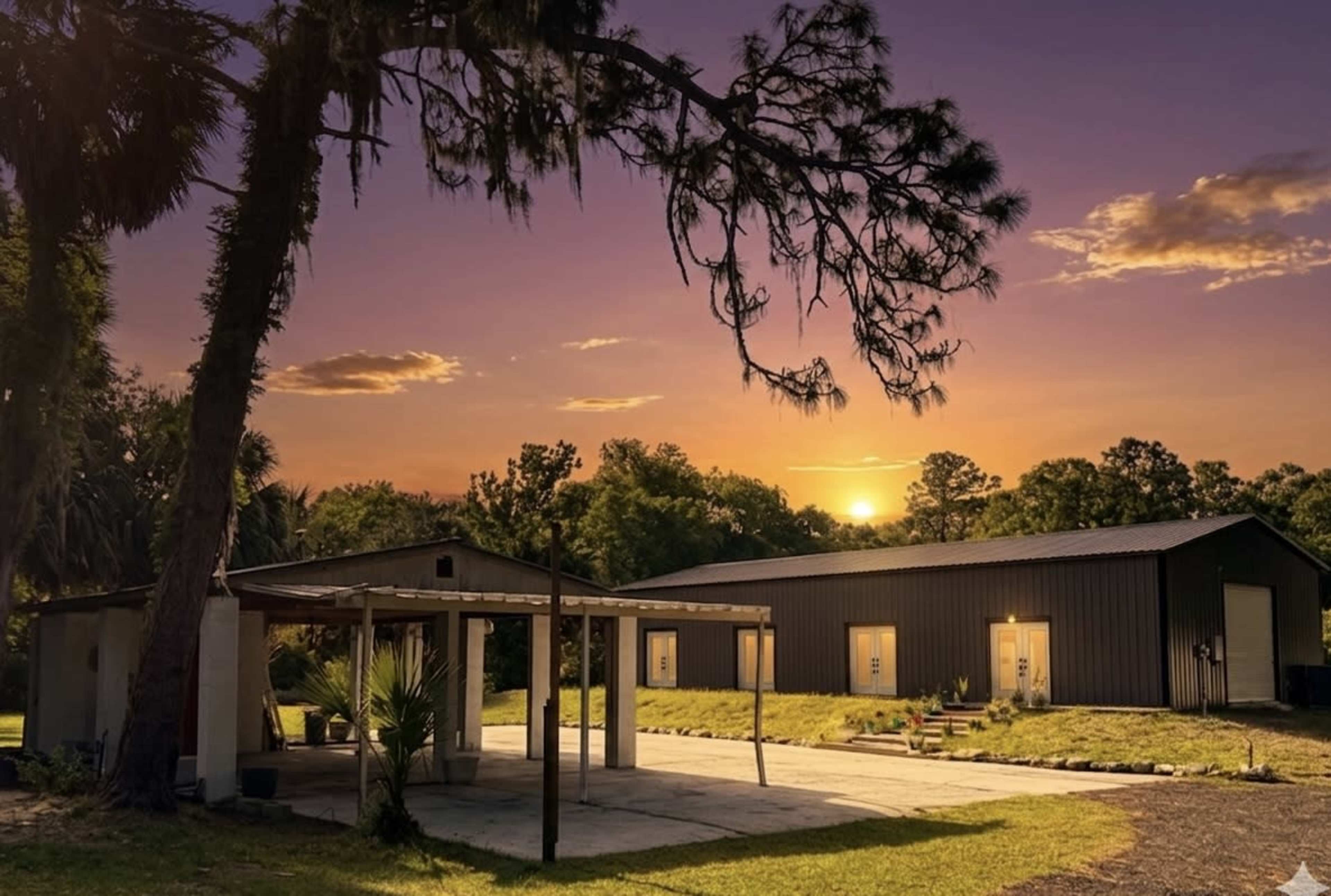 A modern building is set against a sunset backdrop, with trees and a paved area in the foreground.