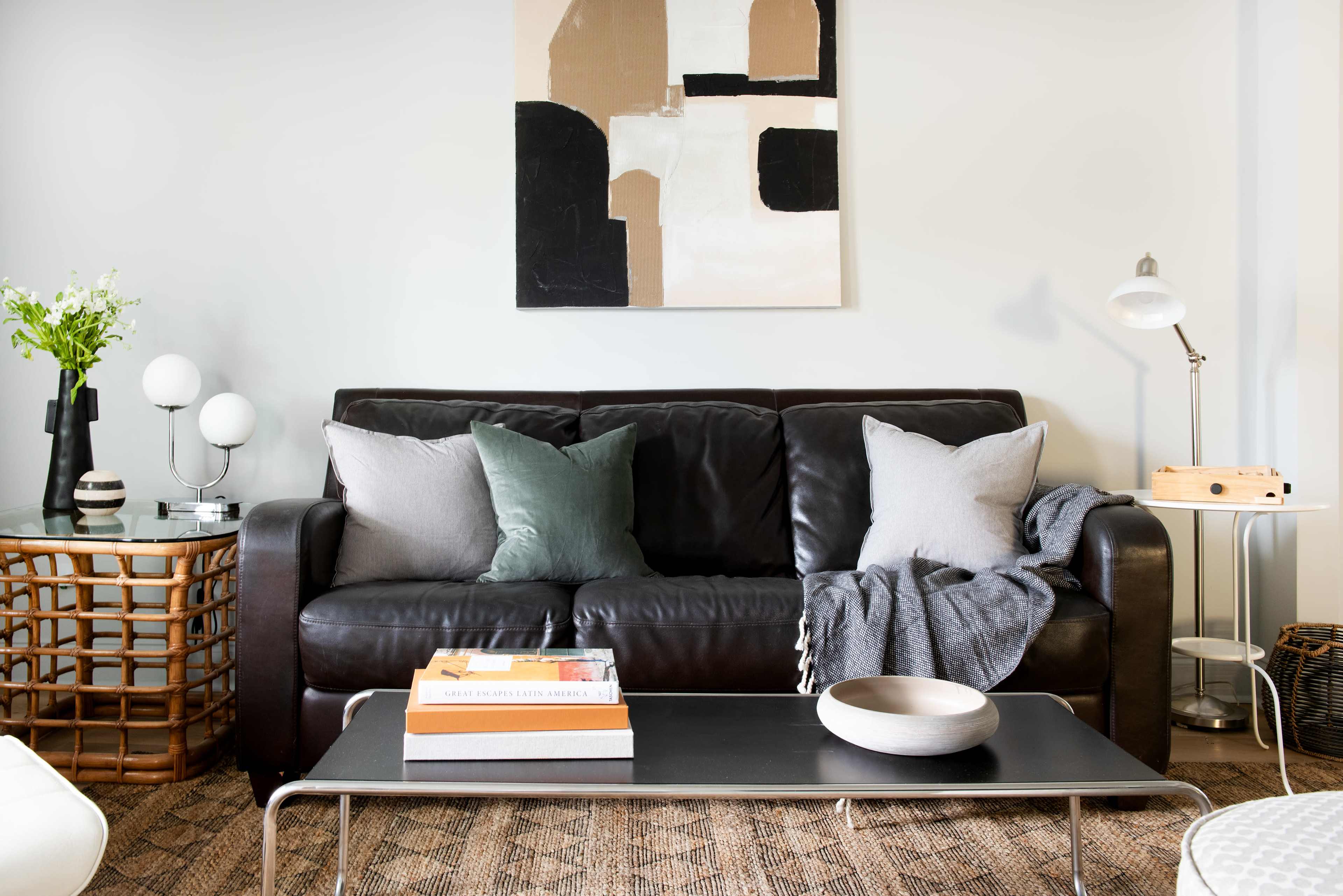 A dark leather sofa is positioned against a wall, adorned with decorative pillows, a throw blanket, and a coffee table topped with magazines and a decorative bowl.
