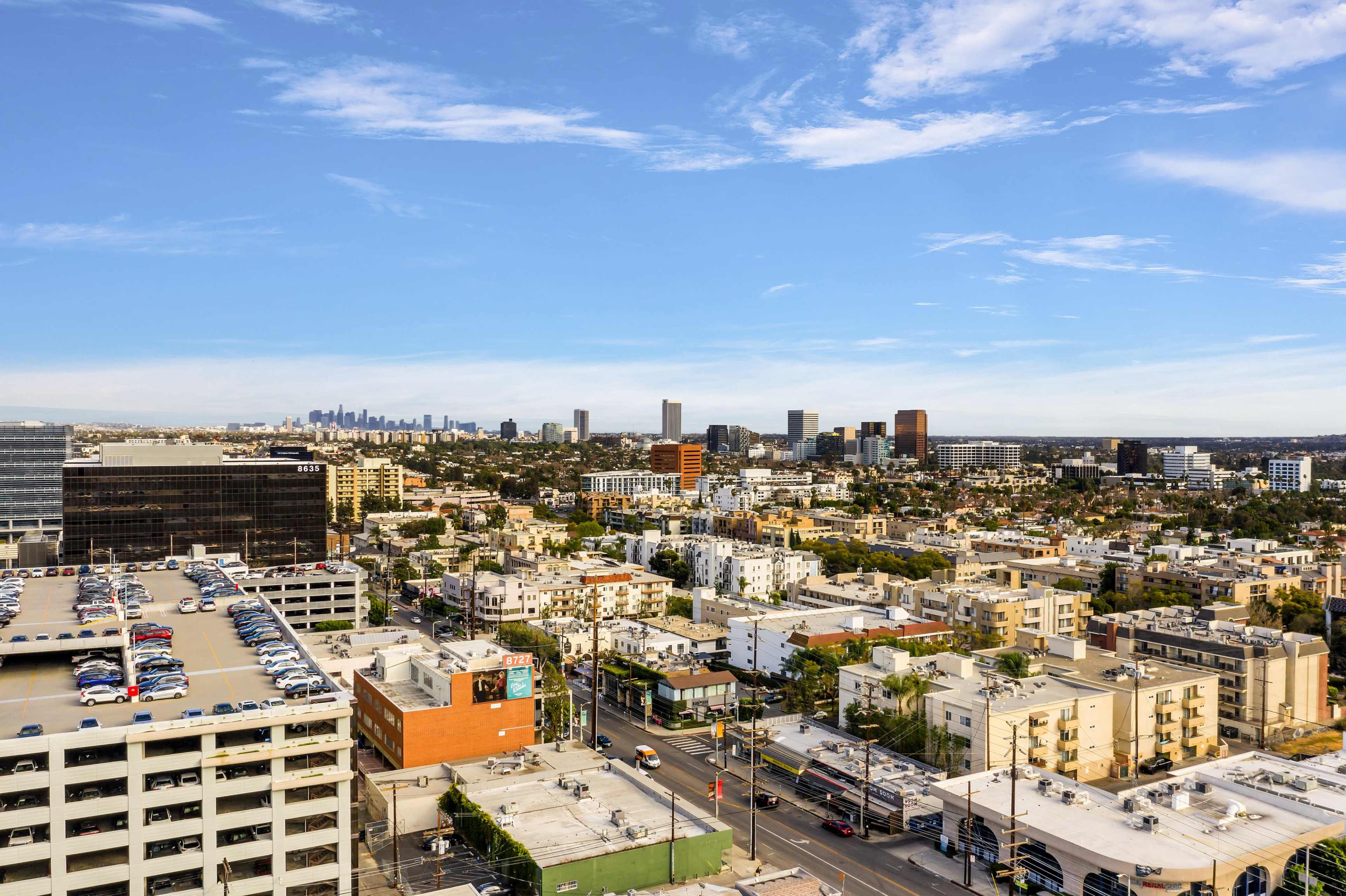 A panoramic view of a city skyline with numerous buildings and a parking structure in the foreground.