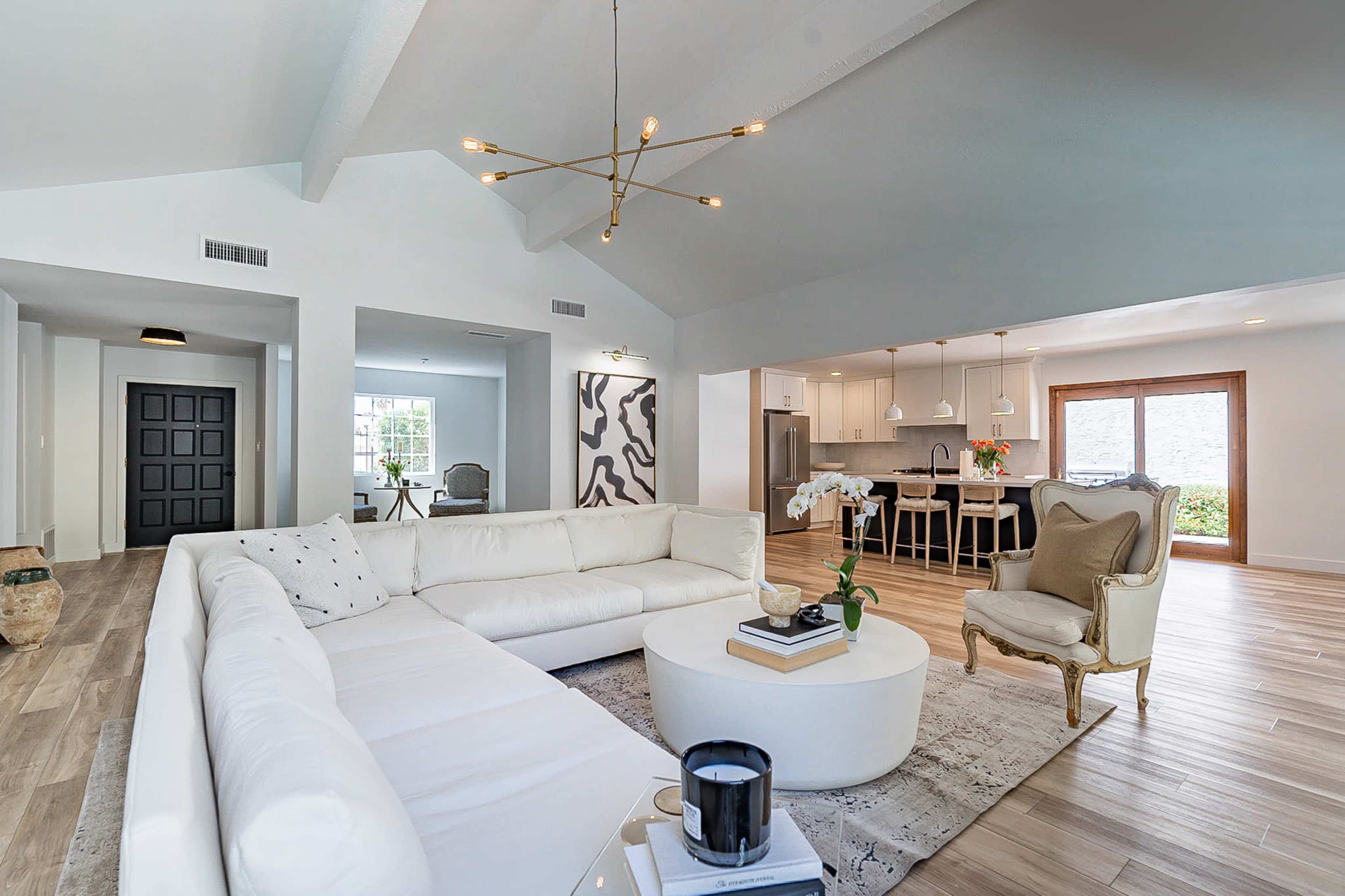 A modern living room with a white sectional sofa, a round coffee table, and a view into an adjoining kitchen area with a dining table.