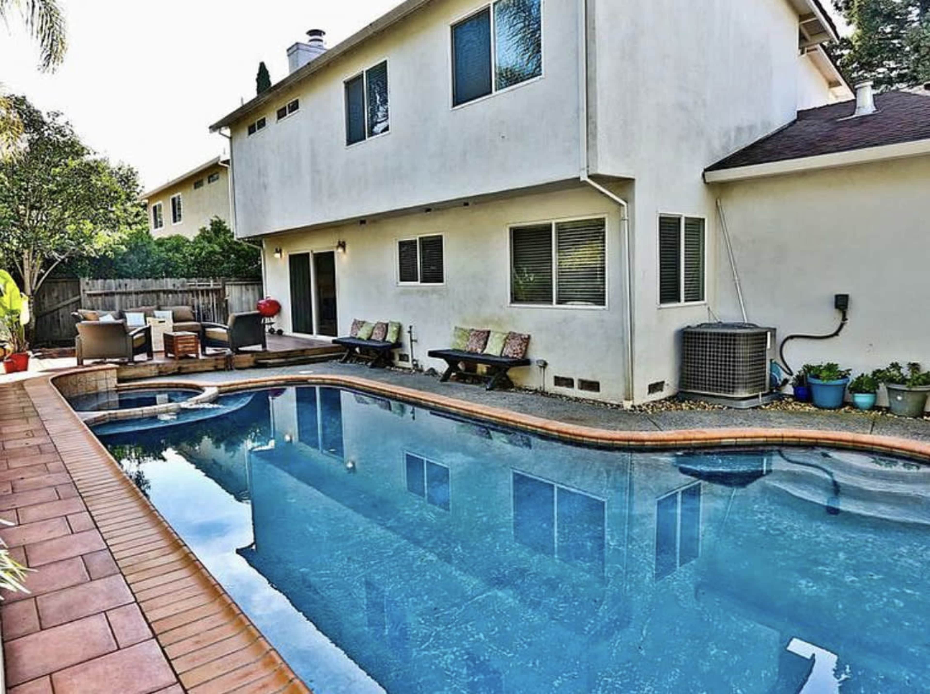 A residential backyard with a swimming pool, lounge chairs, and a house with multiple windows.