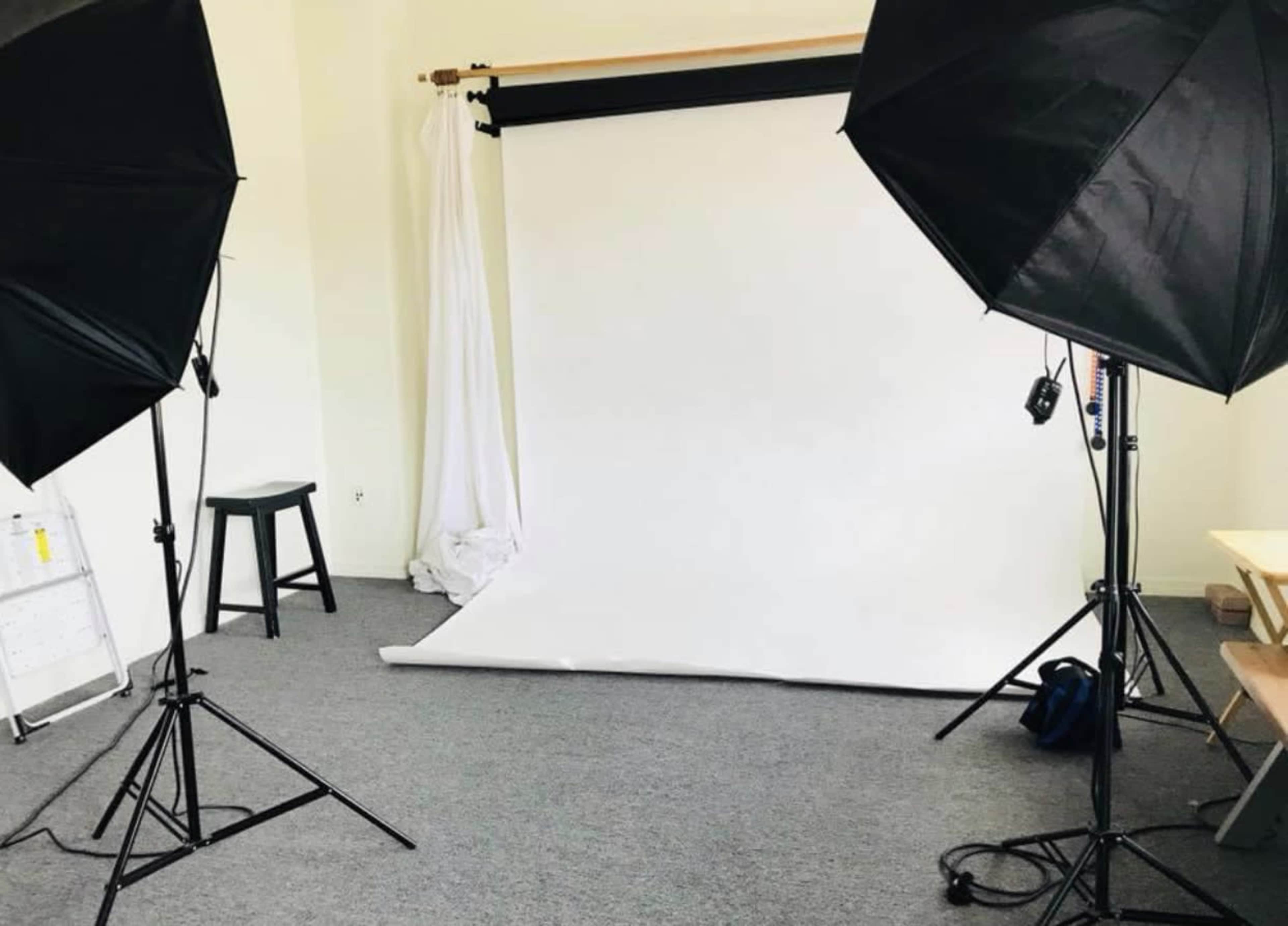 The image shows a photography studio setup with two softbox lights positioned on either side of a white backdrop on the floor.