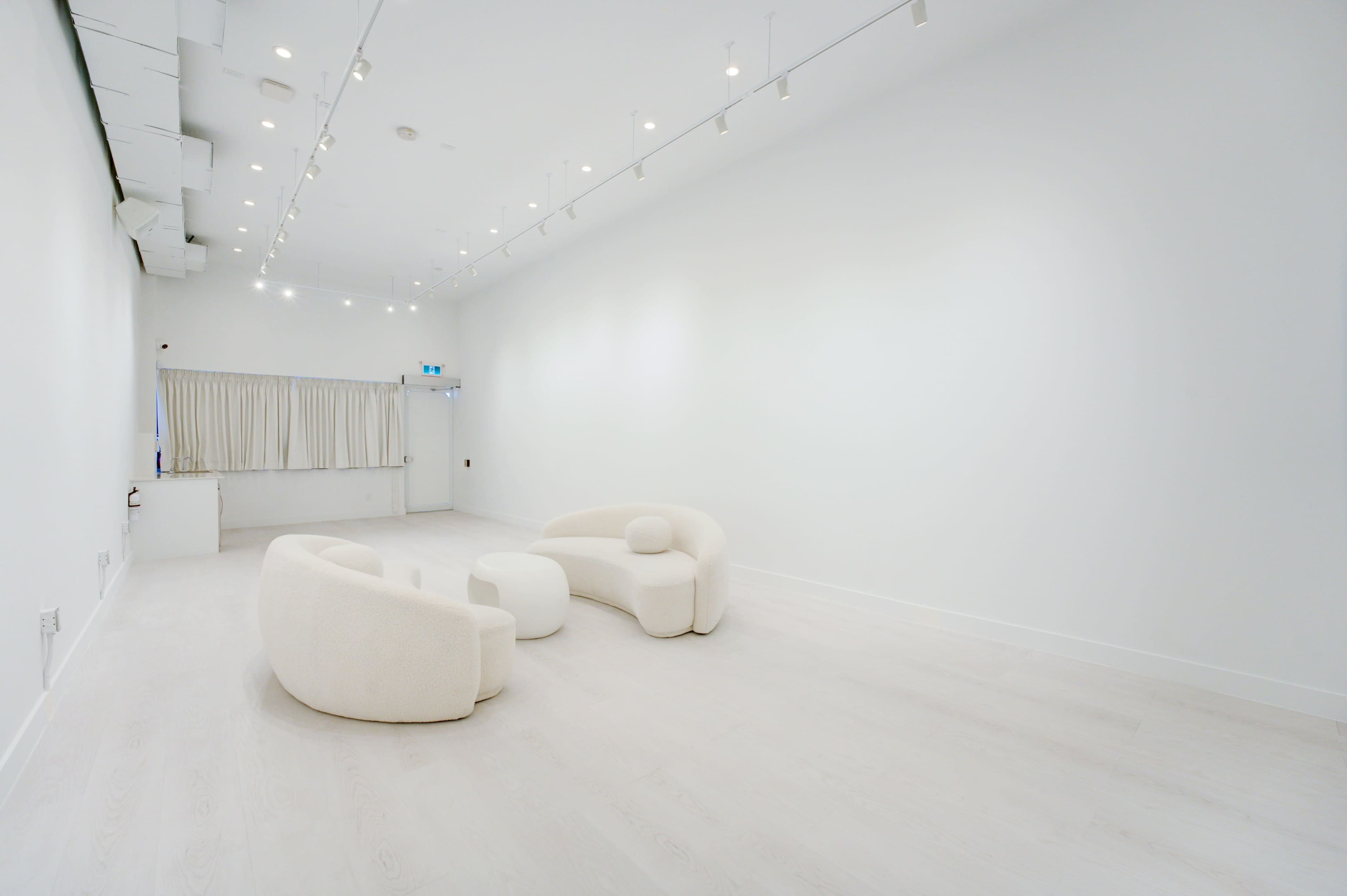 The image features a minimalistic white room with two curved sofas and a round table, illuminated by ceiling lights.