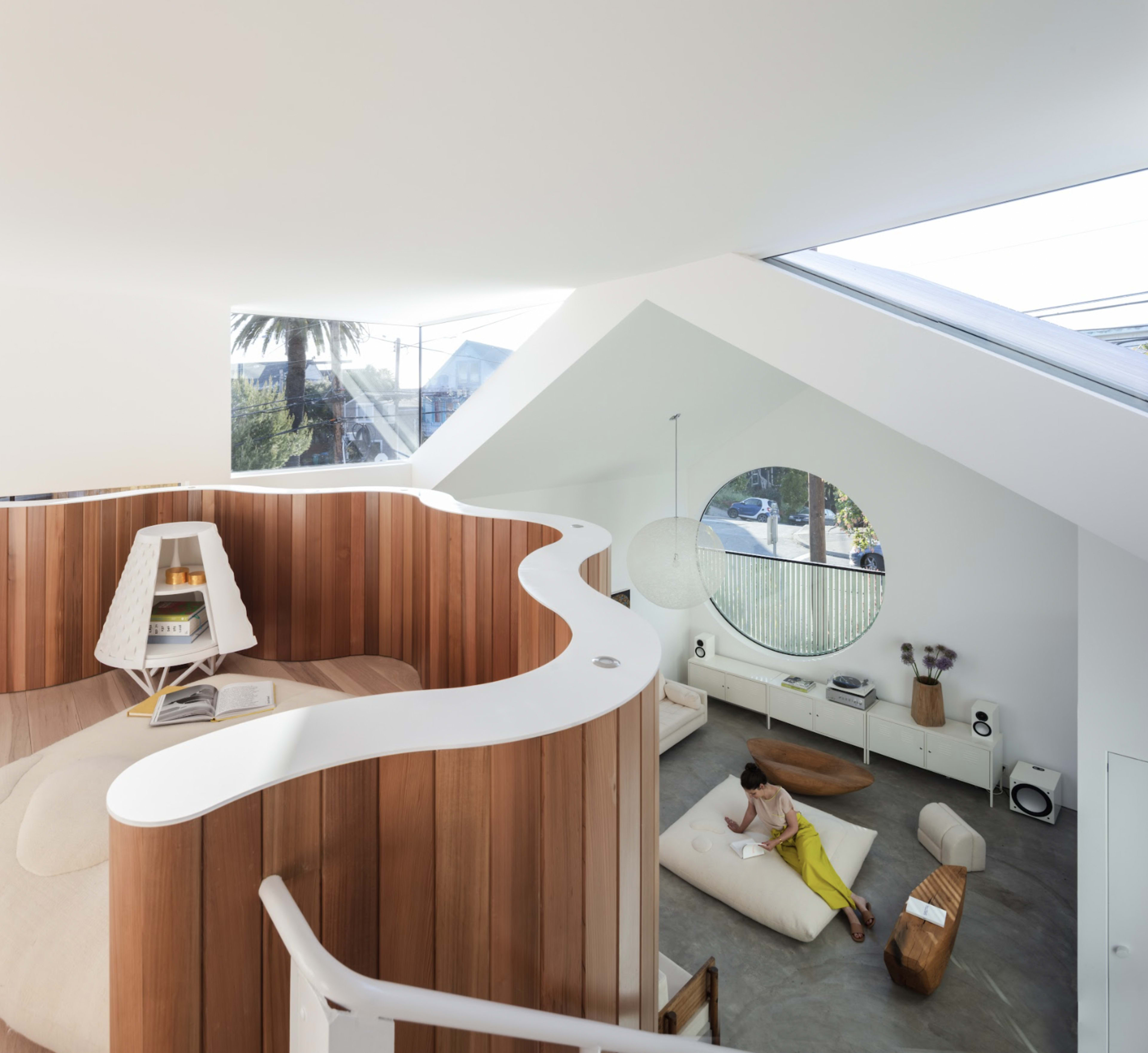 The image shows a modern, open-concept living space with a wooden curved structure and a circular window allowing natural light to enter.