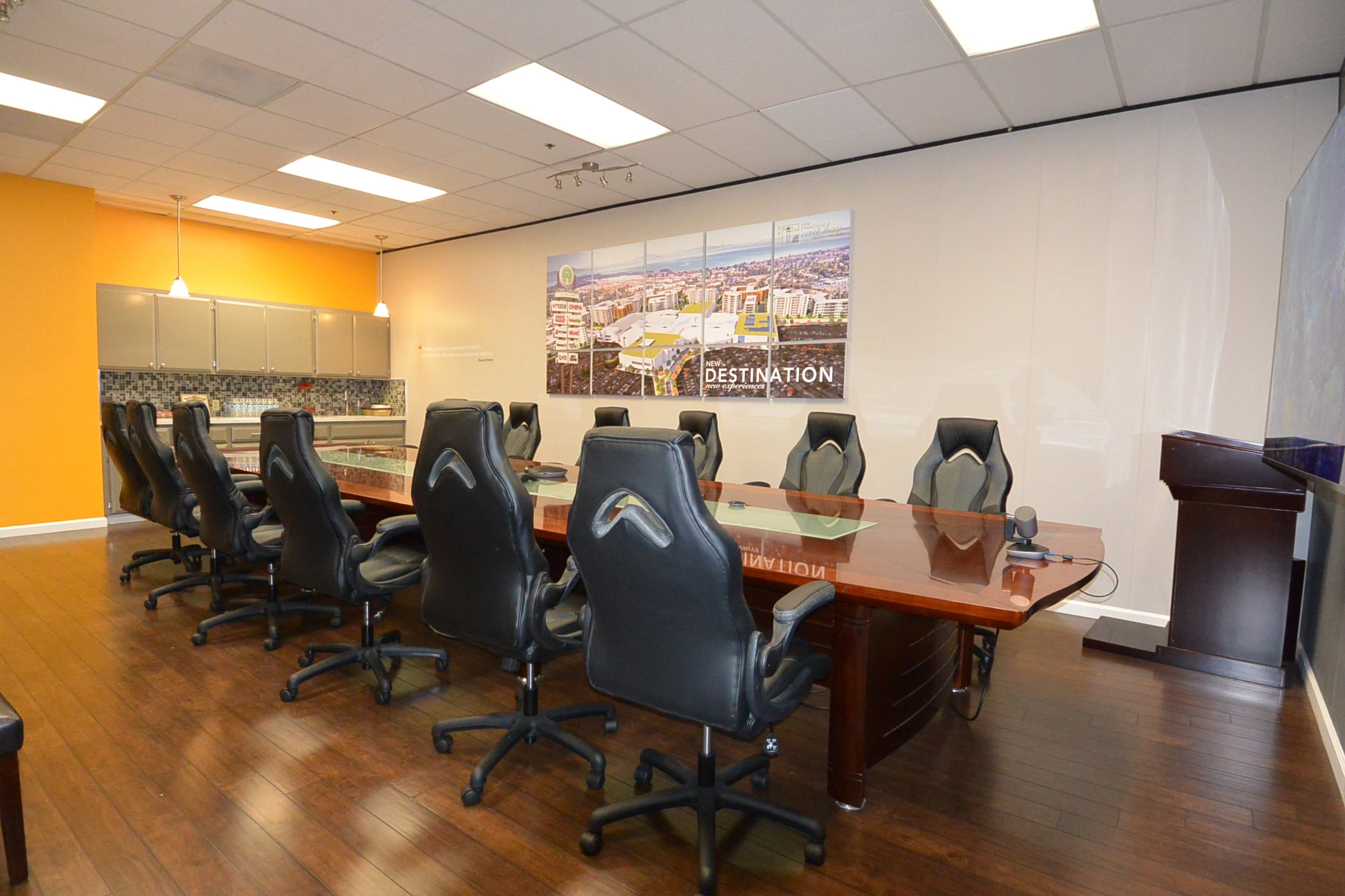 A conference room with a large wooden table and several black ergonomic chairs, featuring a wall display of a cityscape.