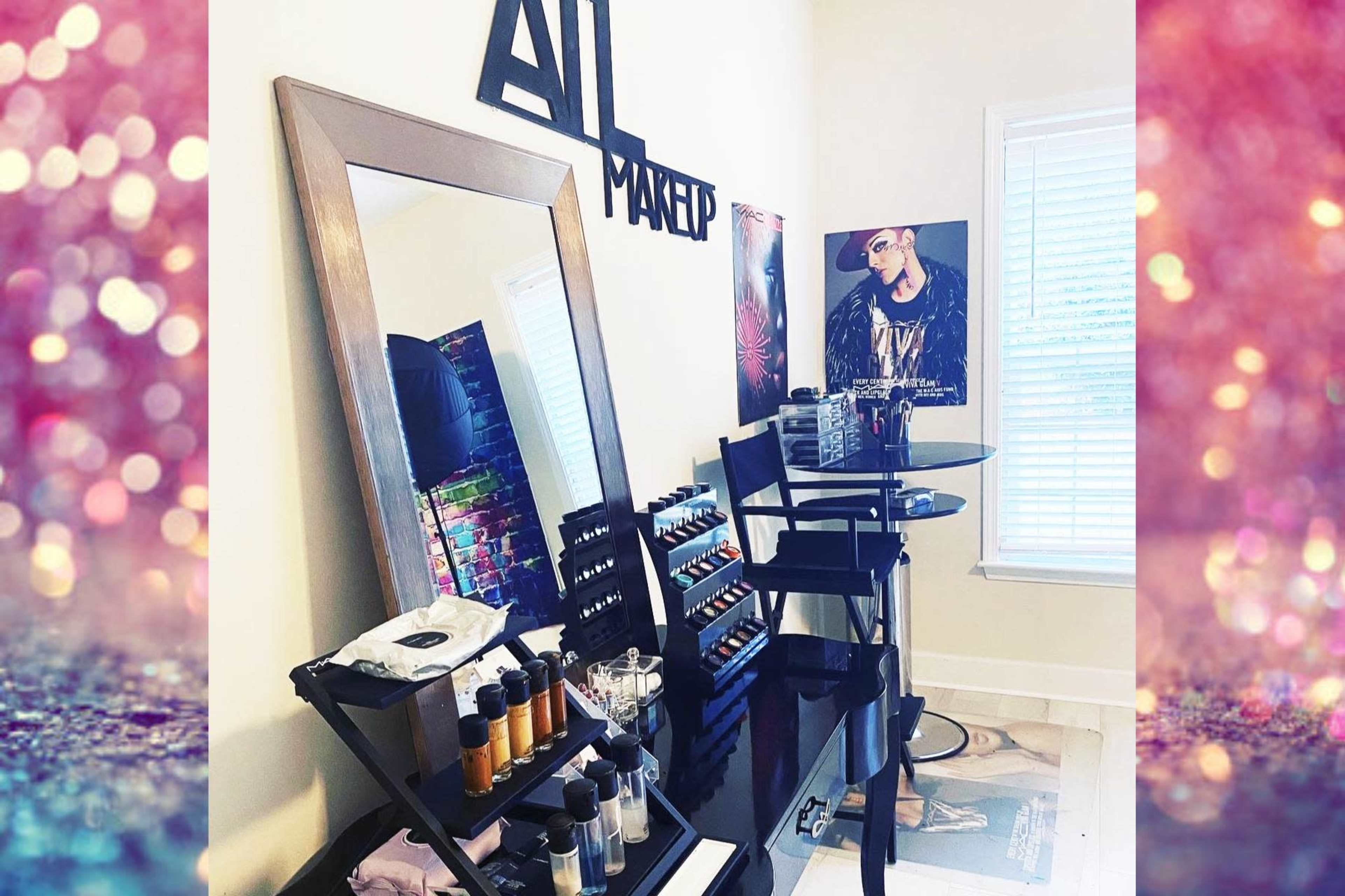 A makeup station featuring a large mirror, a selection of makeup products arranged on a table, and a poster on the wall.