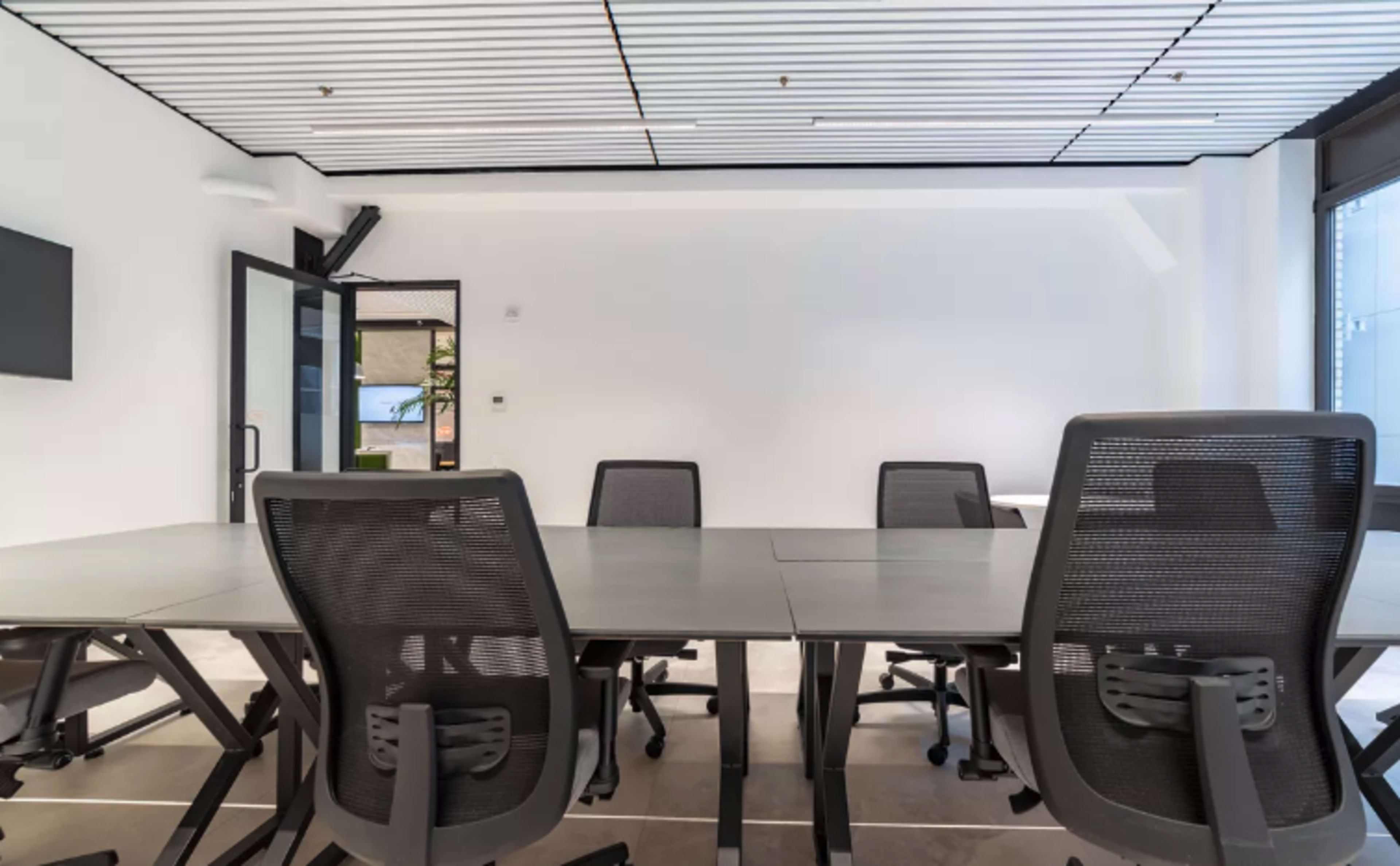 A conference room with a large table and multiple chairs is shown, featuring a minimalist design and a large window.