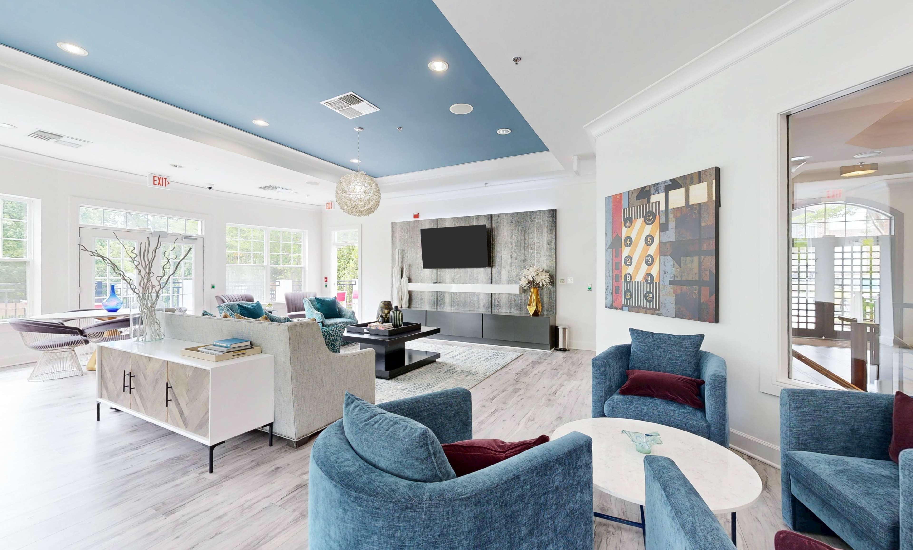 The image shows a modern lounge area with blue and white decor, featuring comfortable seating, a large television, and decorative artwork.