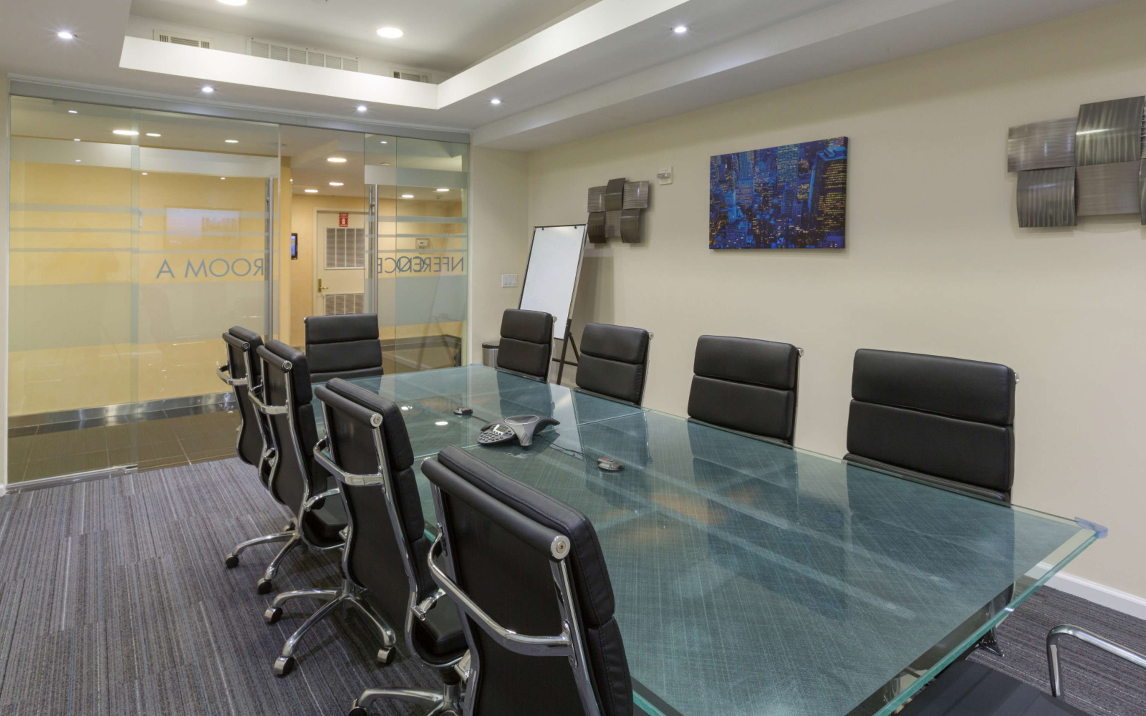 A large conference room features a glass table surrounded by black leather chairs, with a whiteboard and glass partition in the background.