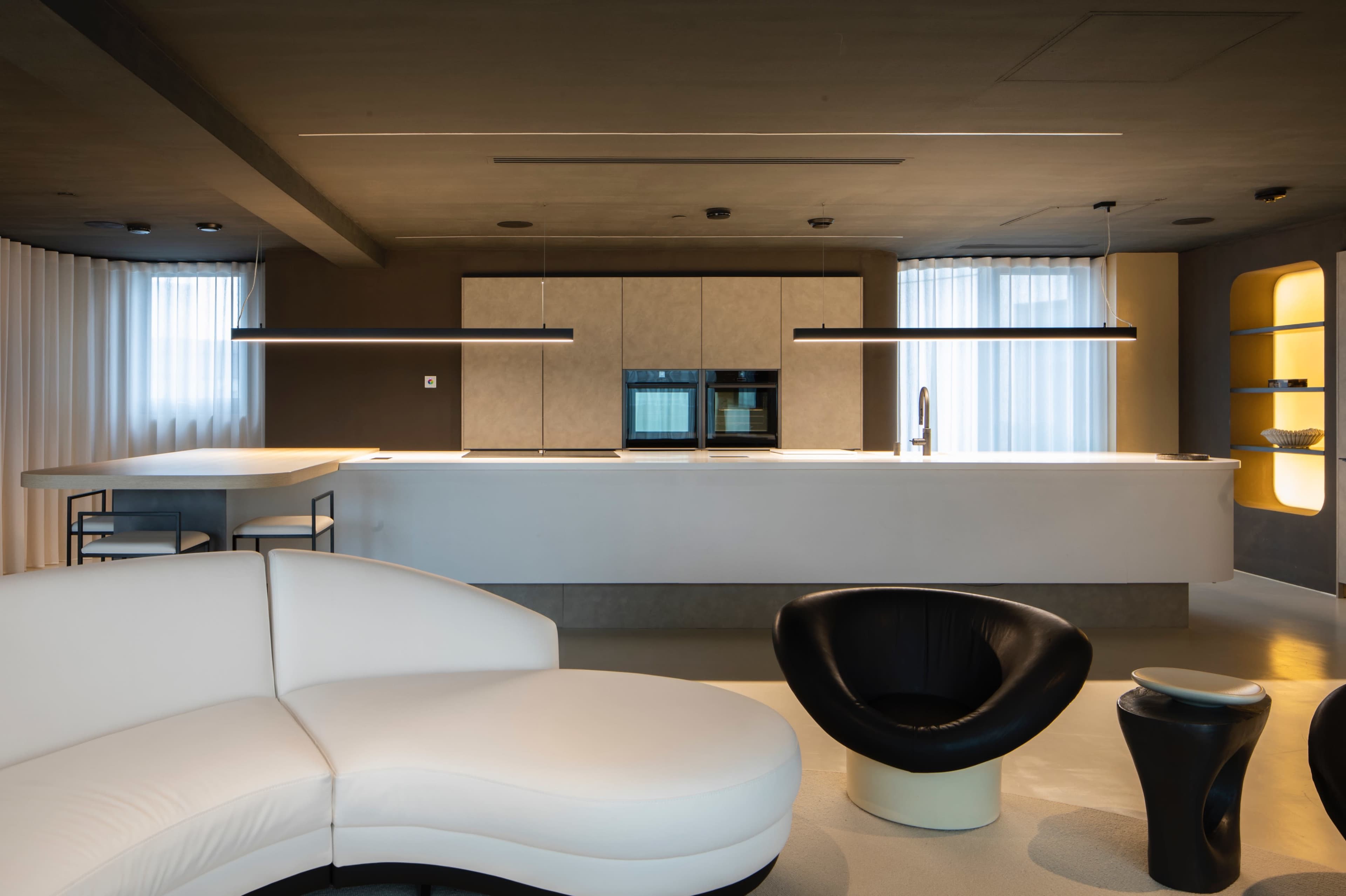 A modern kitchen and living area featuring a curved white sectional sofa, a black chair, and sleek cabinetry with an island countertop.