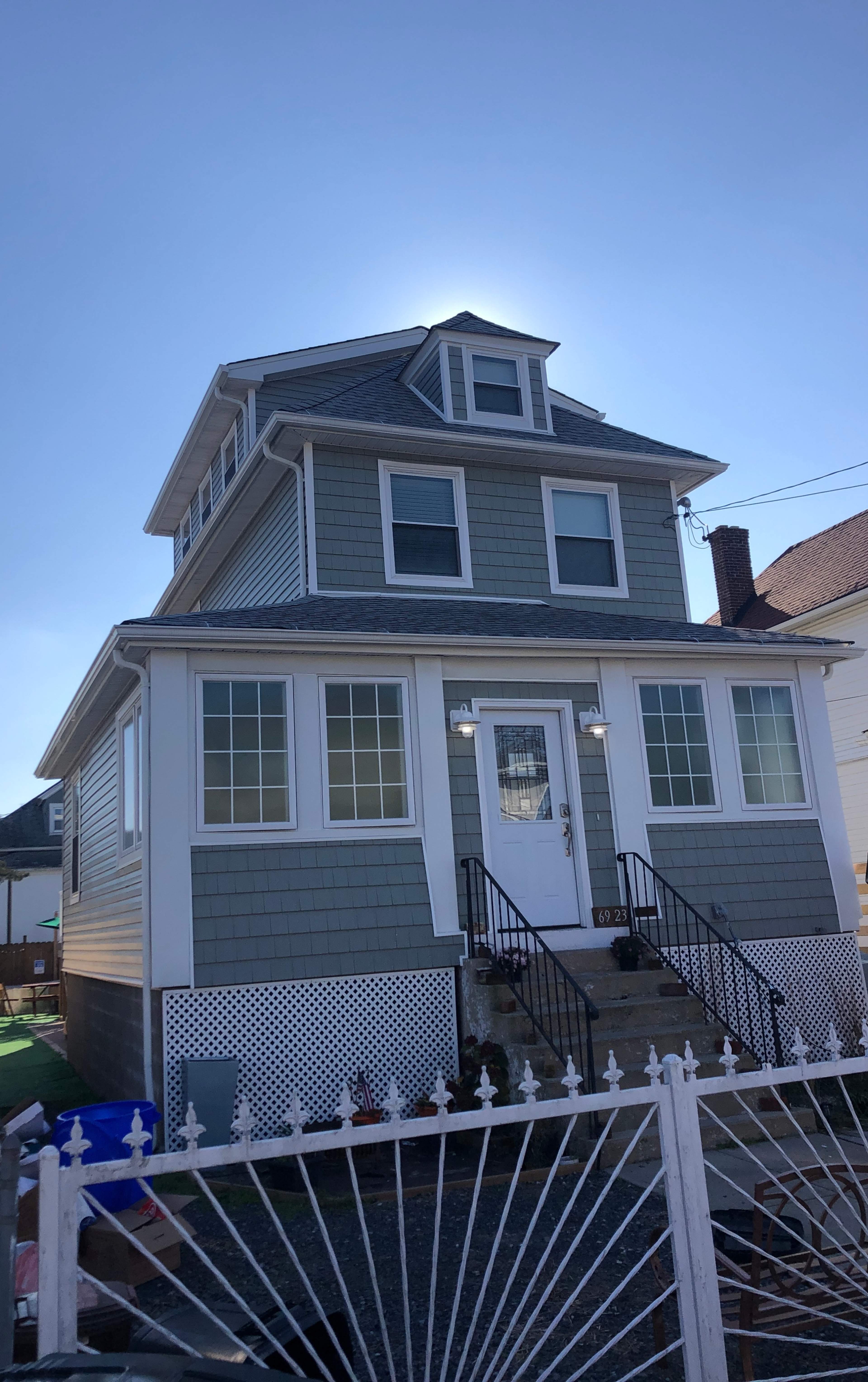 A three-story house with gray siding and white trim features a central entrance and multiple windows.