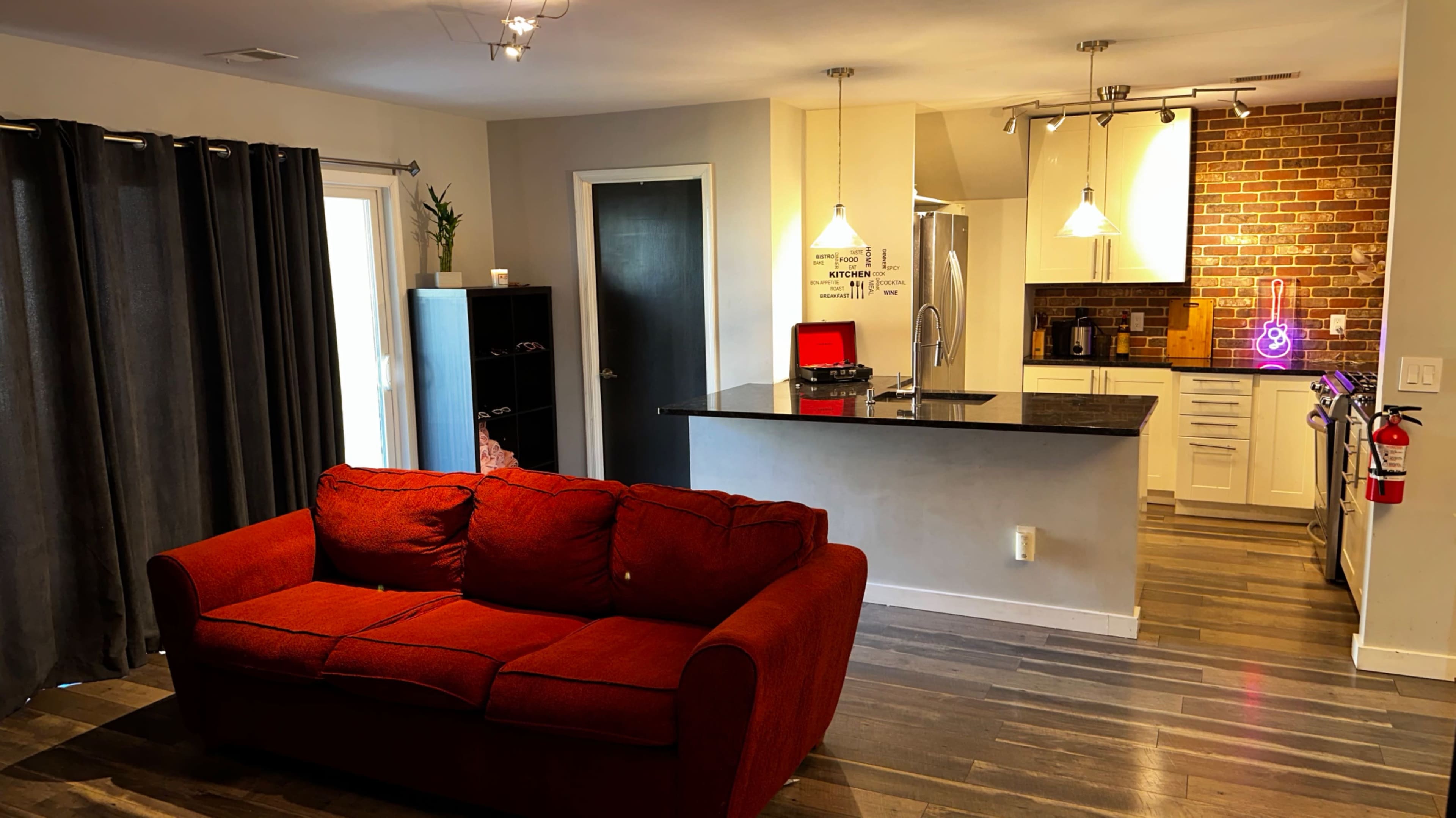 A modern living area with a red couch facing an open kitchen featuring a brick backsplash and stainless steel appliances.