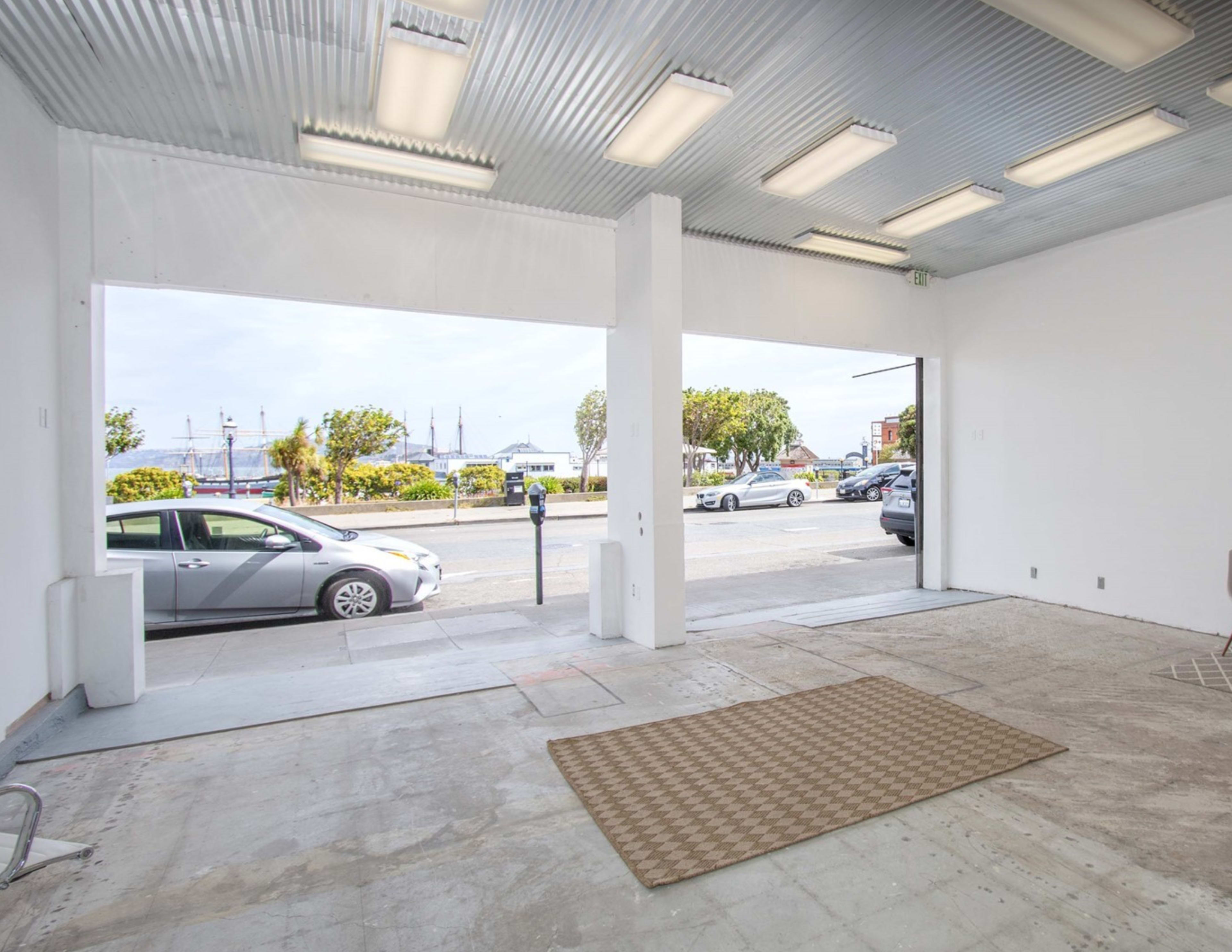 The image shows an empty garage space with a view of a street and parked cars outside.