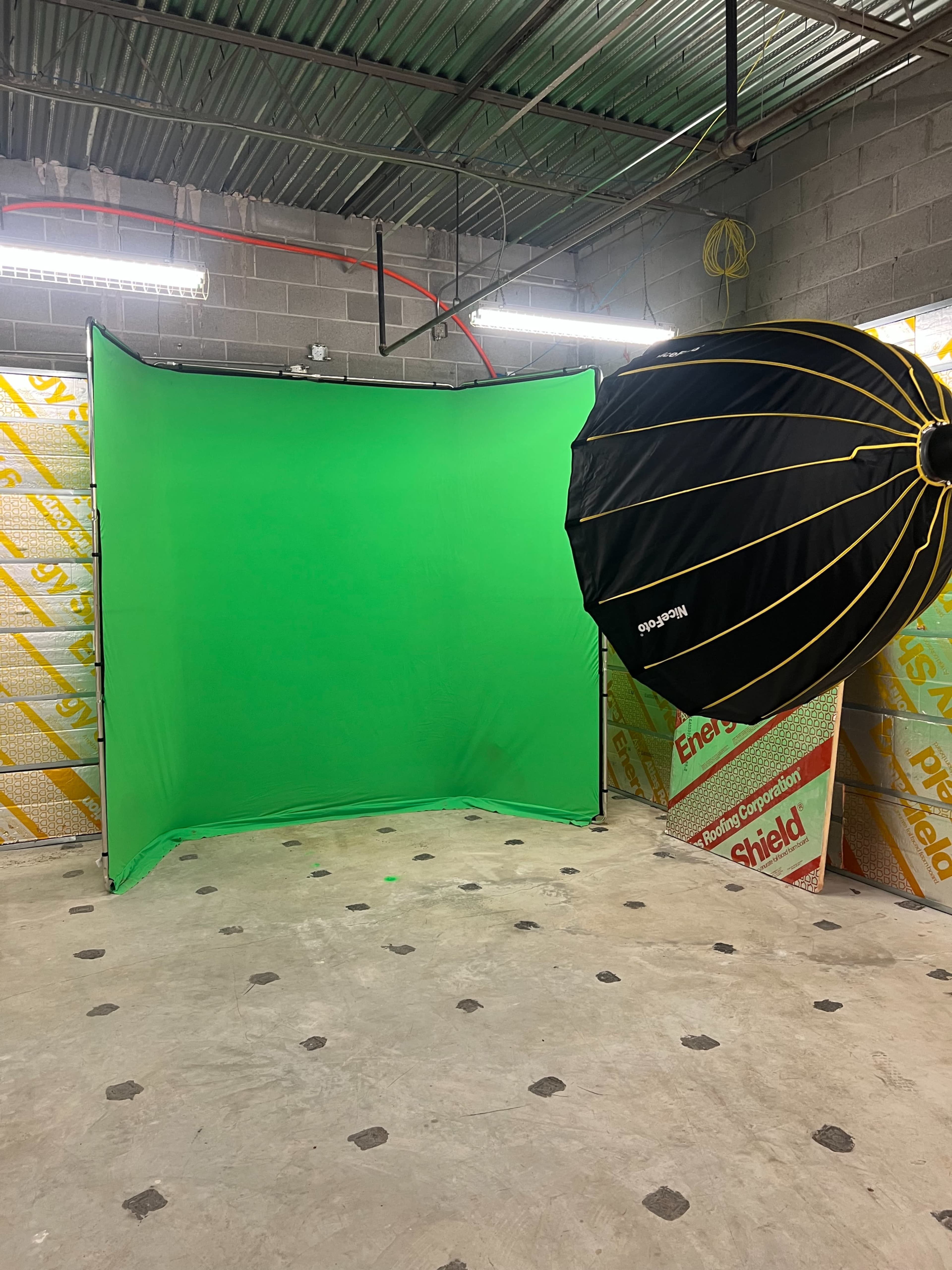 The image shows a green screen setup in an indoor space, with a large softbox light positioned nearby.