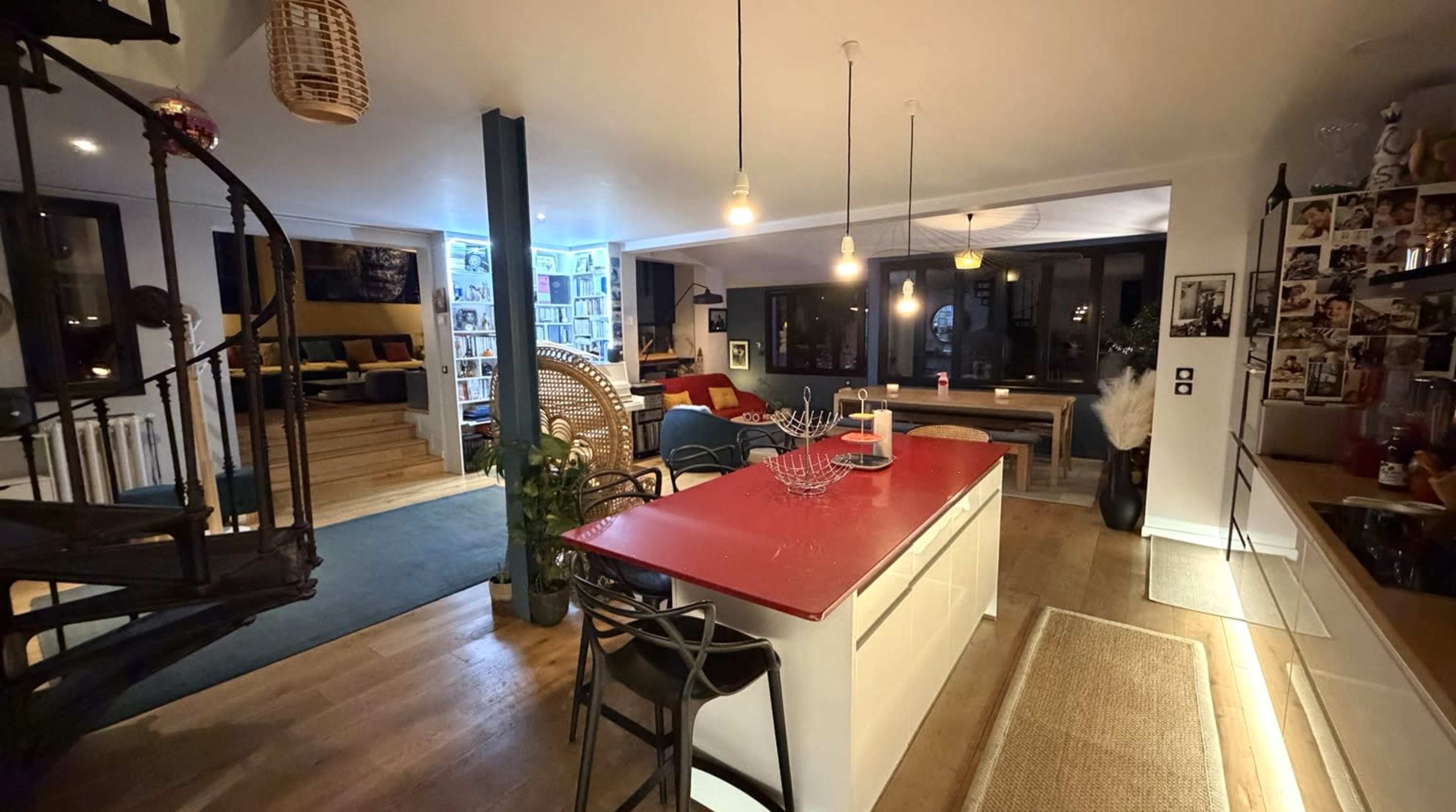 The image shows a modern open-concept kitchen and living area with a spiral staircase and a large bookshelf in the background.