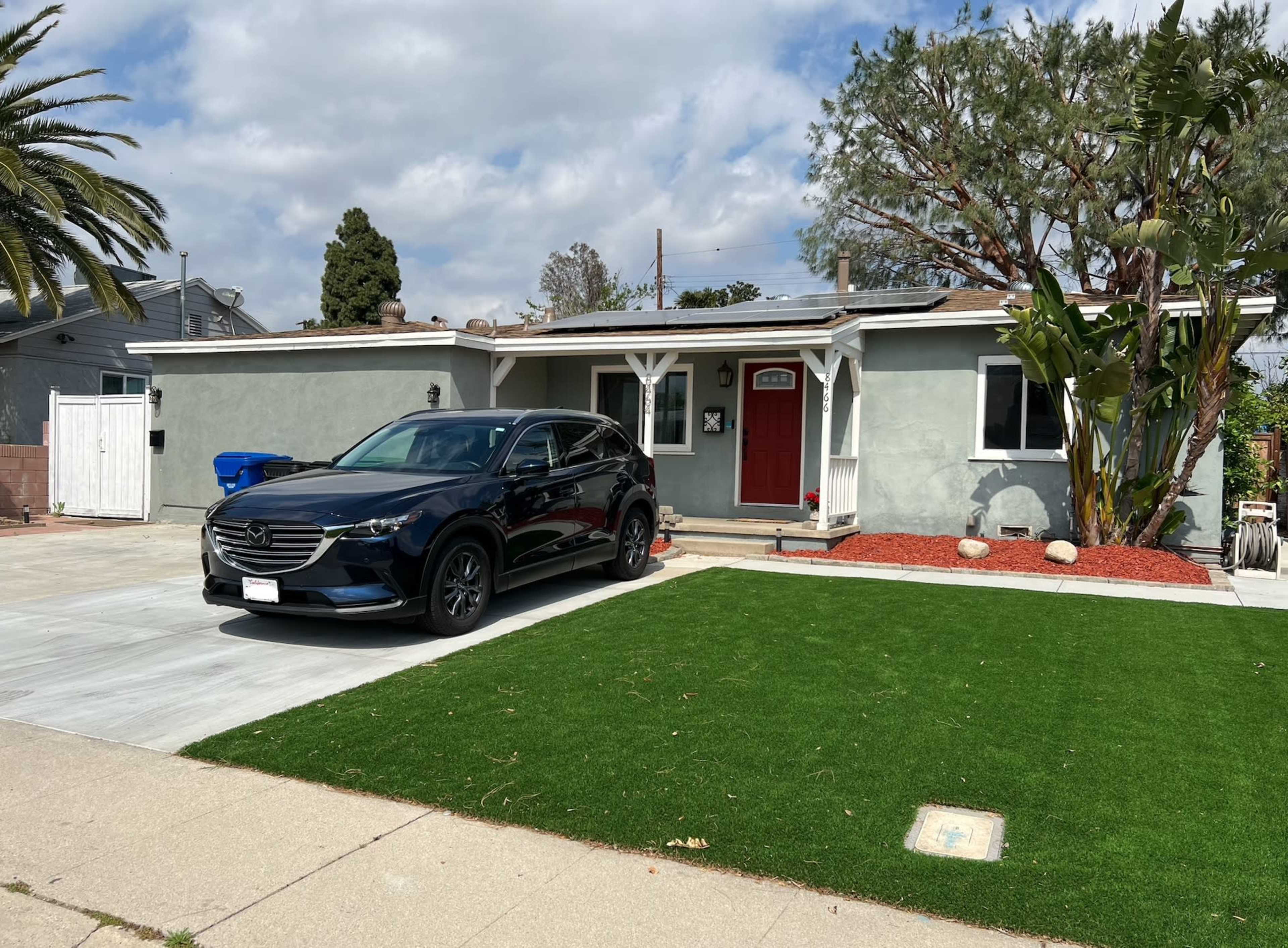 A black SUV is parked on a concrete driveway in front of a single-story house with a red door and a green lawn.