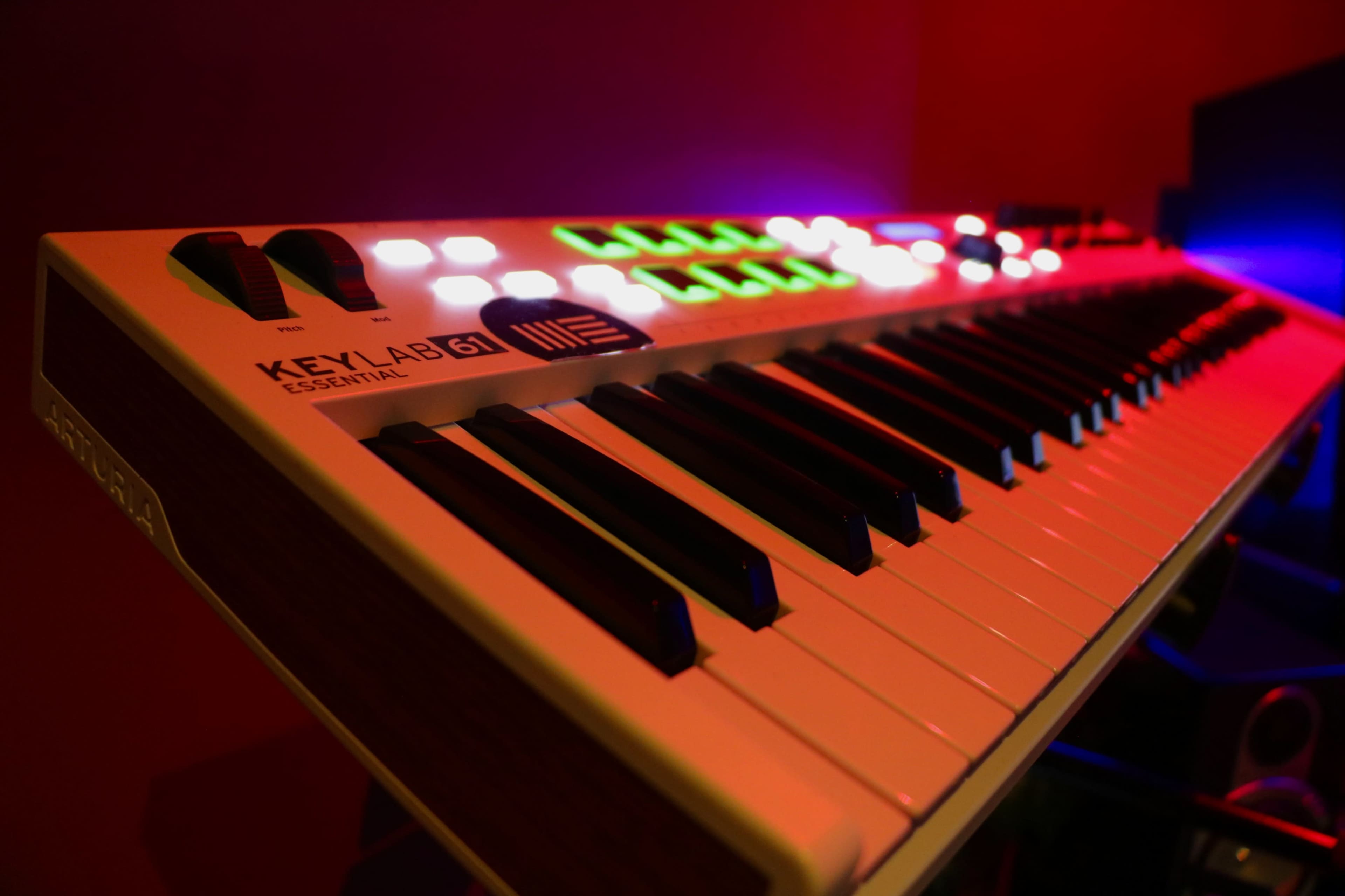 The image shows a close-up of a MIDI keyboard with illuminated buttons and keys against a dark background.