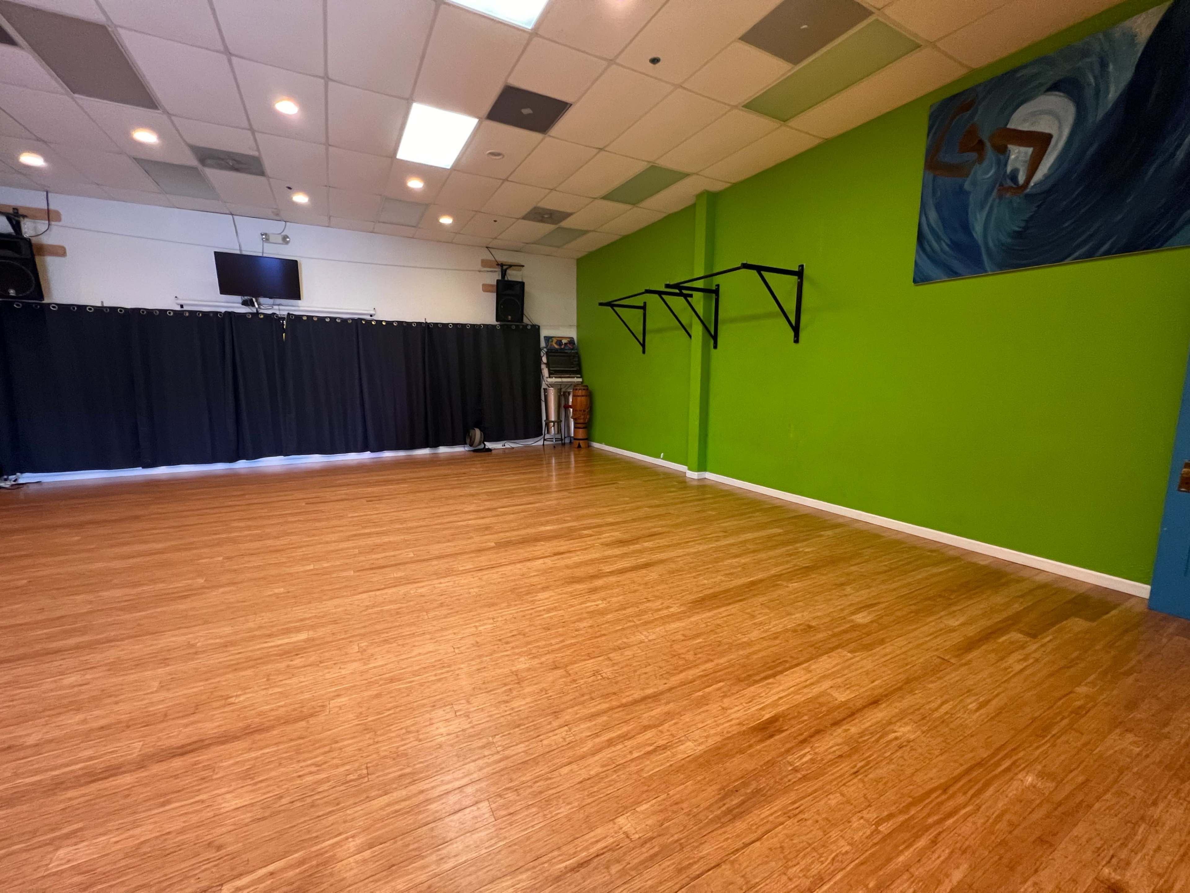 An empty studio space with wooden flooring, green walls, and a black curtain partially drawn at one end.