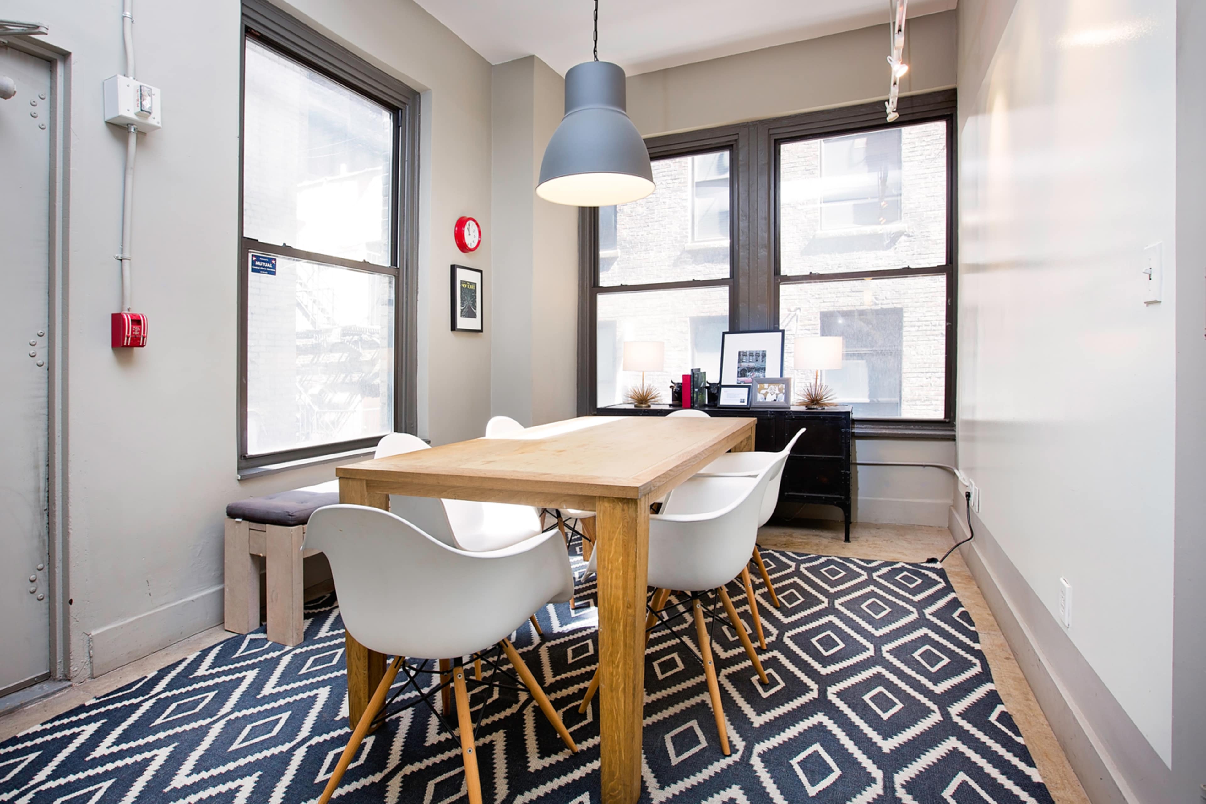 A modern dining area features a wooden table surrounded by white chairs, with large windows allowing natural light to fill the space.