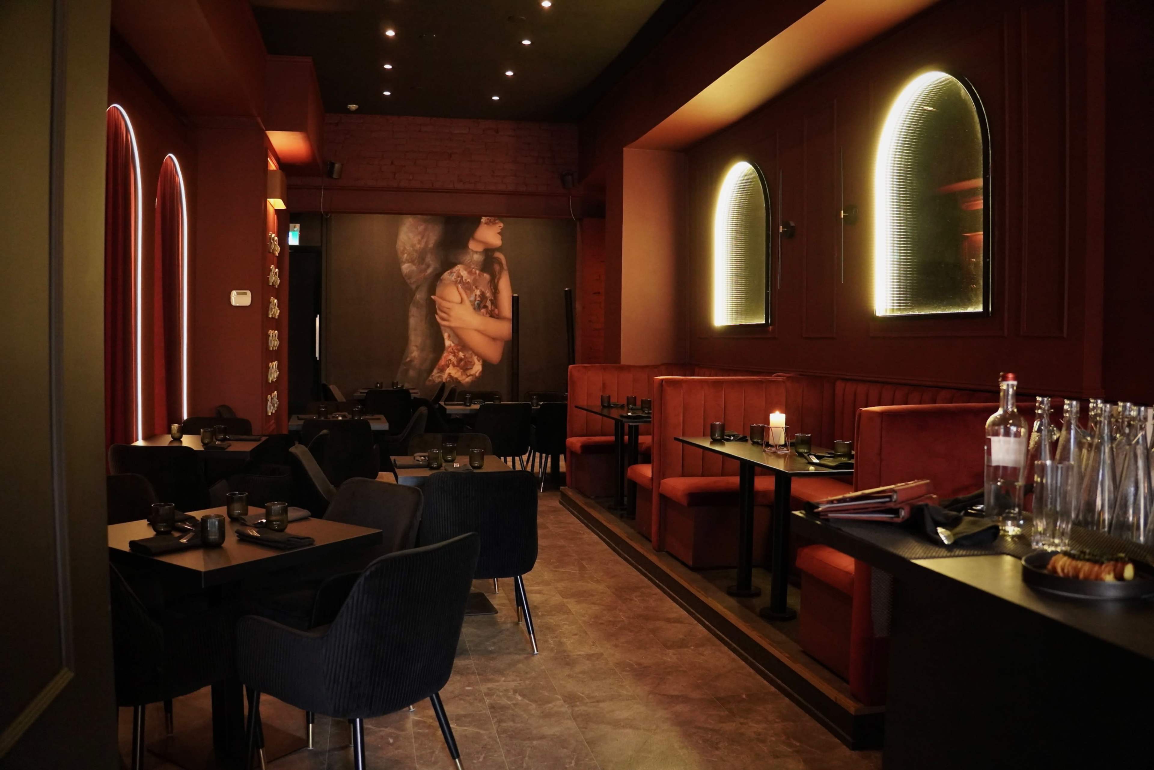 The interior of a stylish restaurant features dark walls, red seating, and ambient lighting, creating an intimate dining atmosphere.