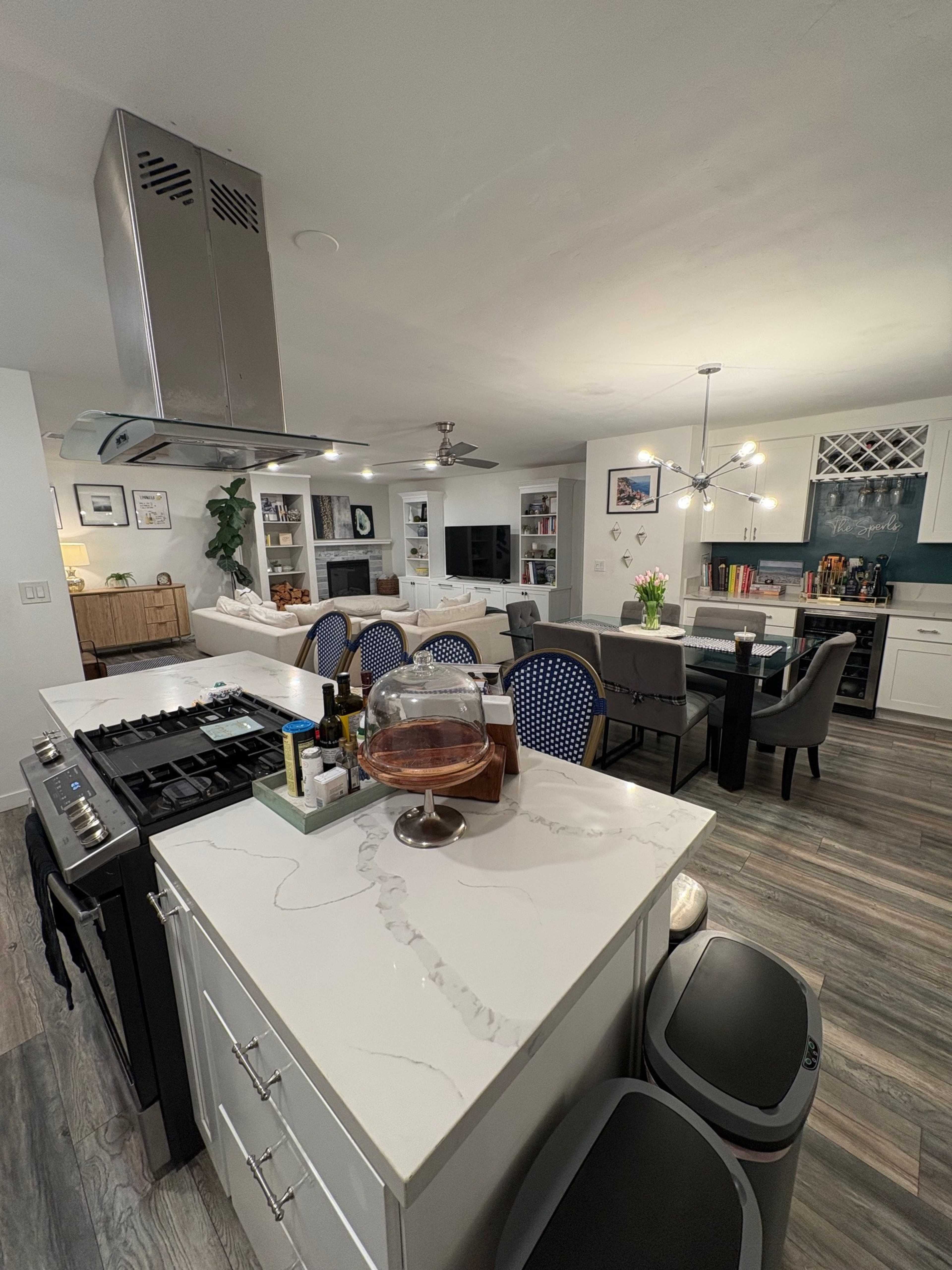 The image shows a modern kitchen with a central island, stainless steel appliances, and a dining area visible in the background.