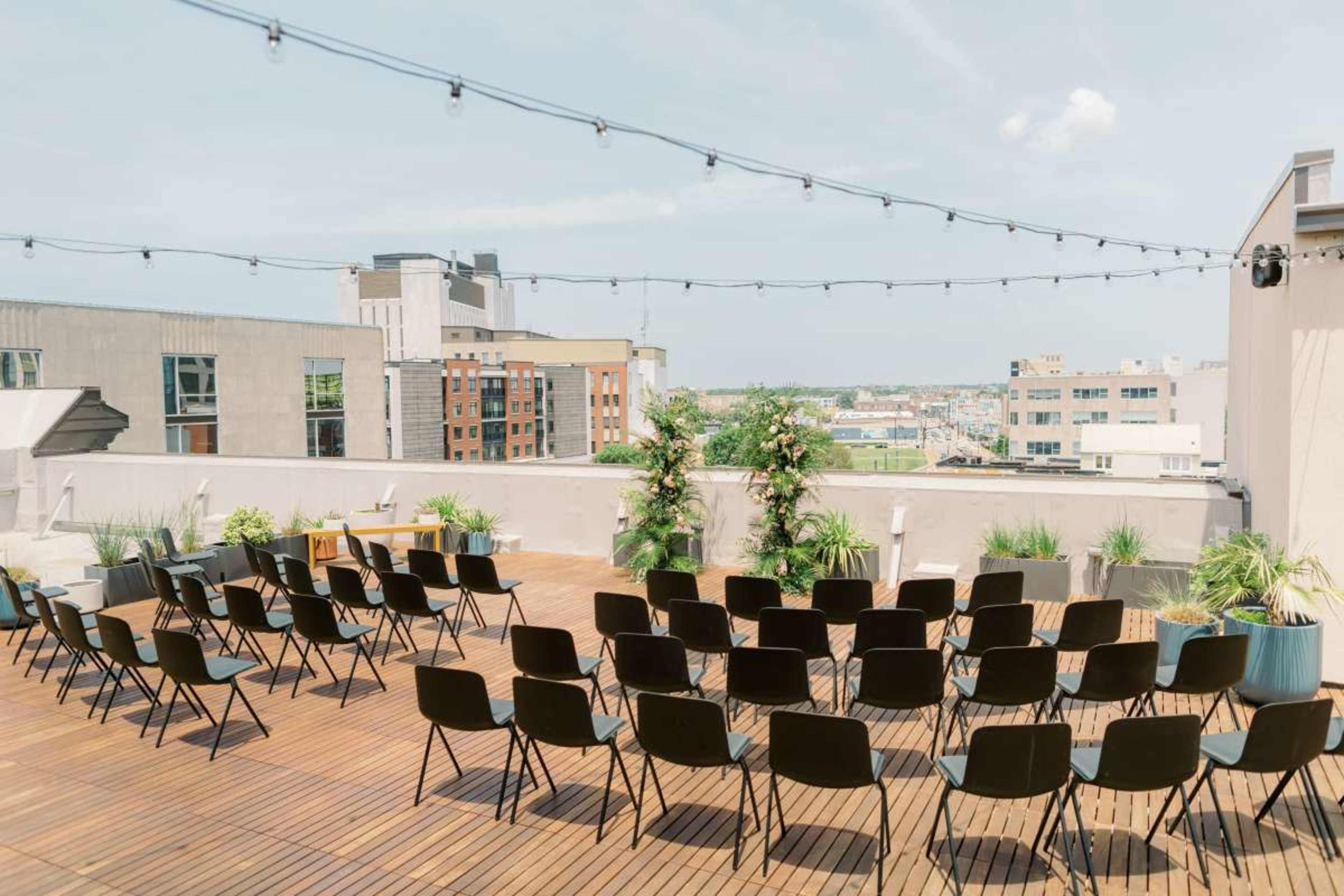 The image shows a rooftop venue arranged with multiple black chairs facing a scenic view of city buildings under a clear sky.