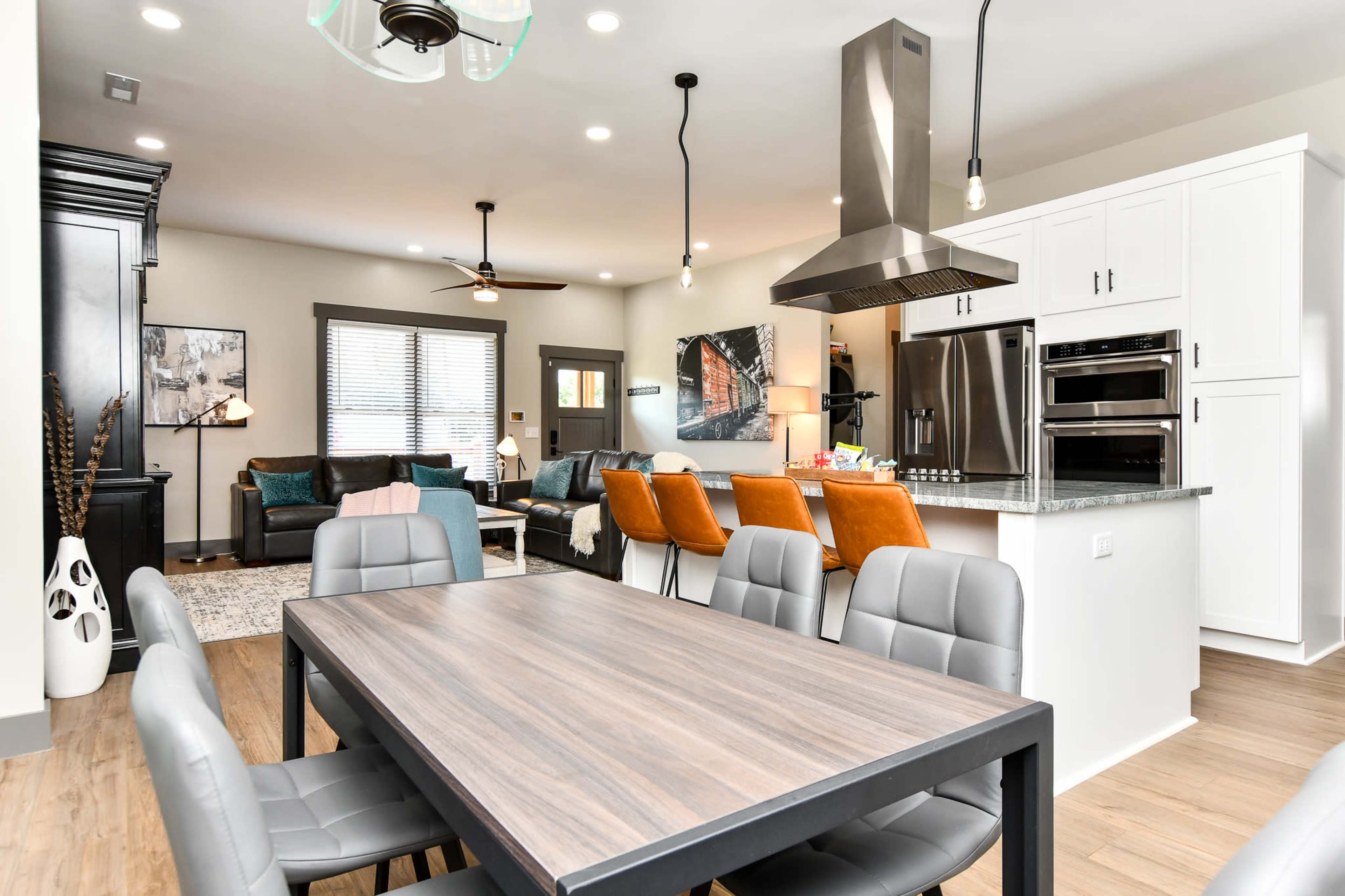 A modern open-concept living and dining area with a dining table in the foreground, a kitchen with stainless steel appliances, and a cozy seating arrangement in the background.