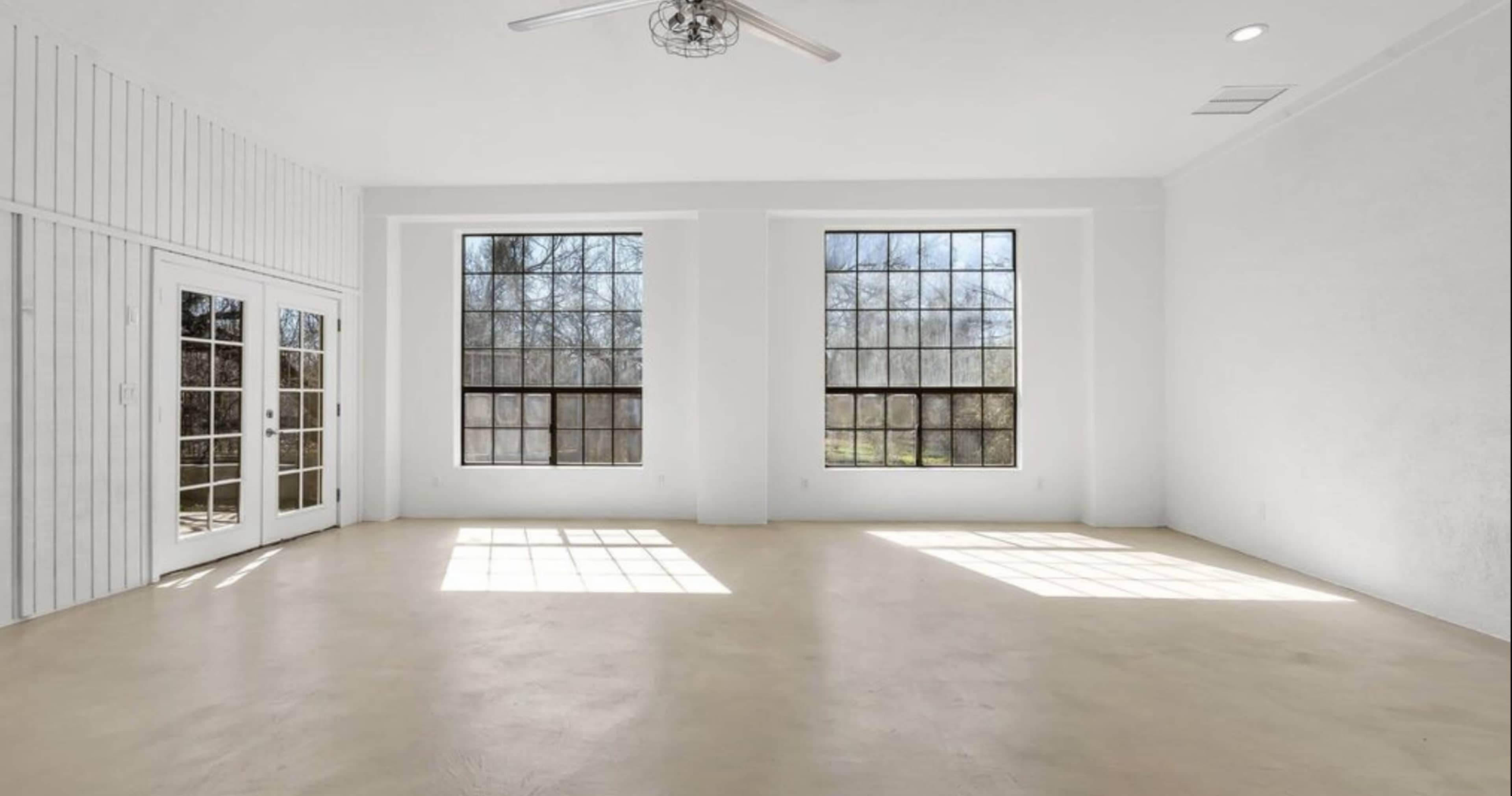 A bright, empty room features large windows and a light-colored concrete floor.