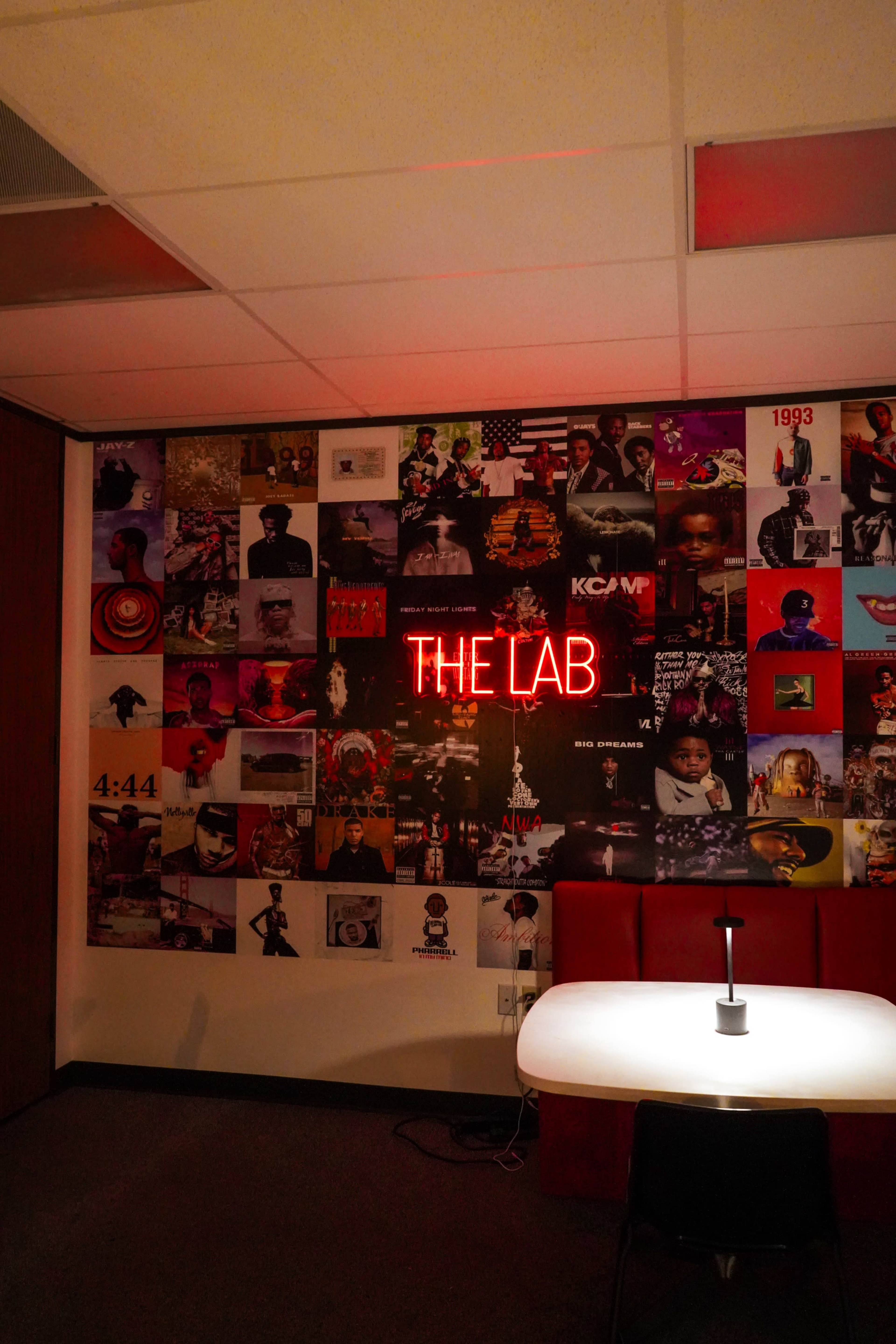 A wall adorned with various music album covers features a bright neon sign that reads "THE LAB."