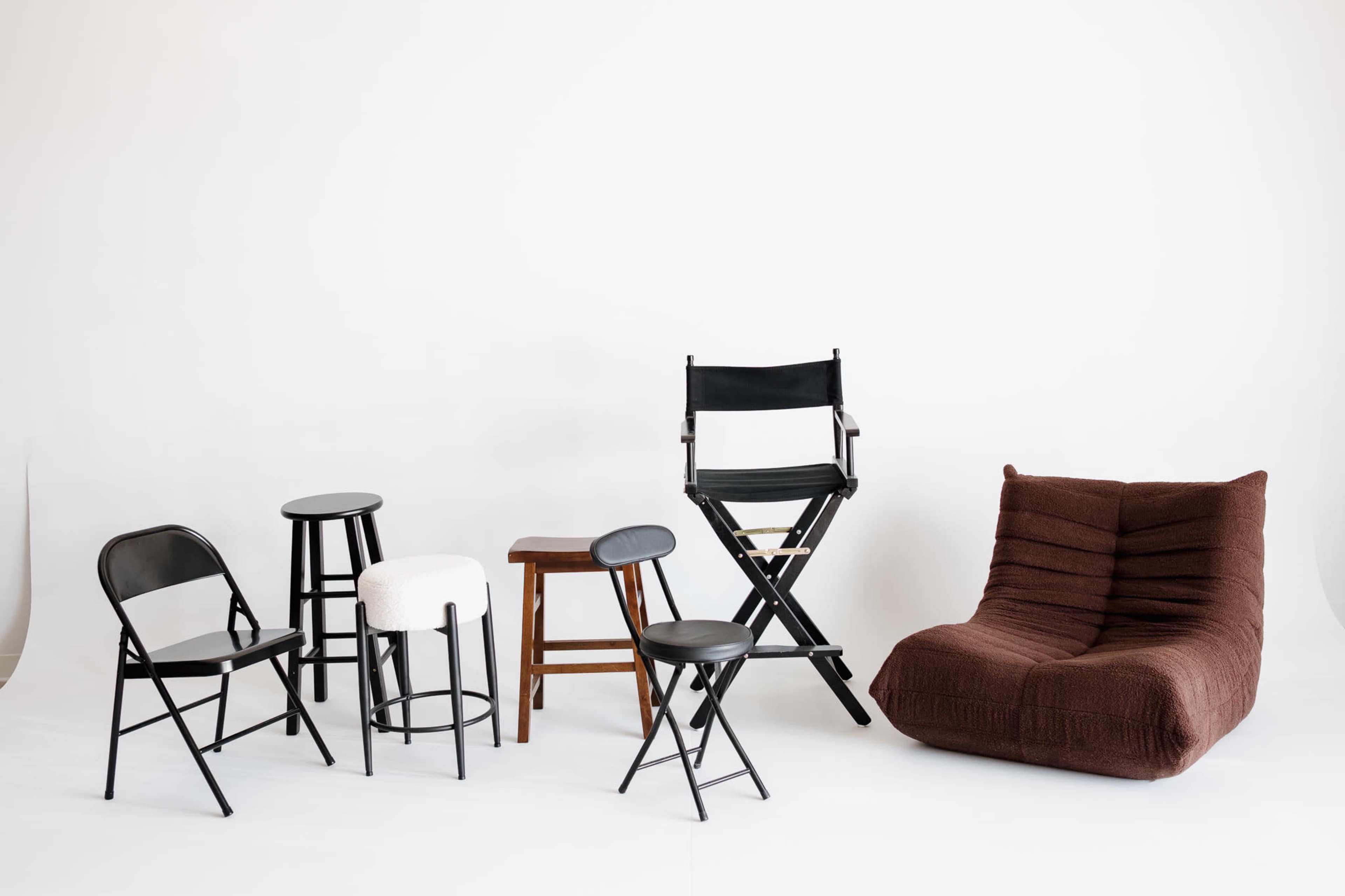 The image features a variety of seating options, including several chairs and stools in different styles and colors, arranged against a plain white background.