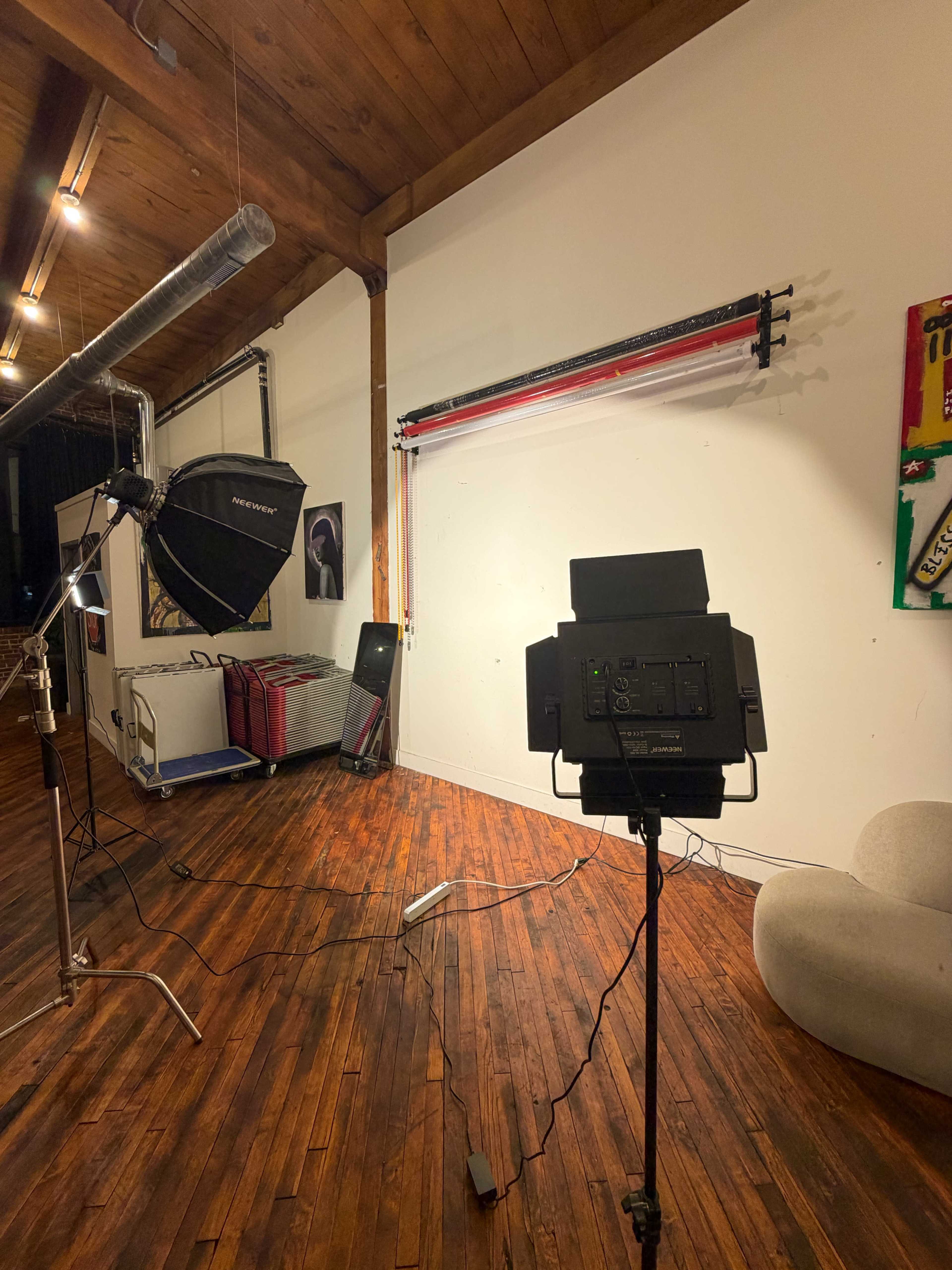 The image shows a photography studio with a large softbox light, a backdrop setup, and wooden flooring illuminated by overhead lights.