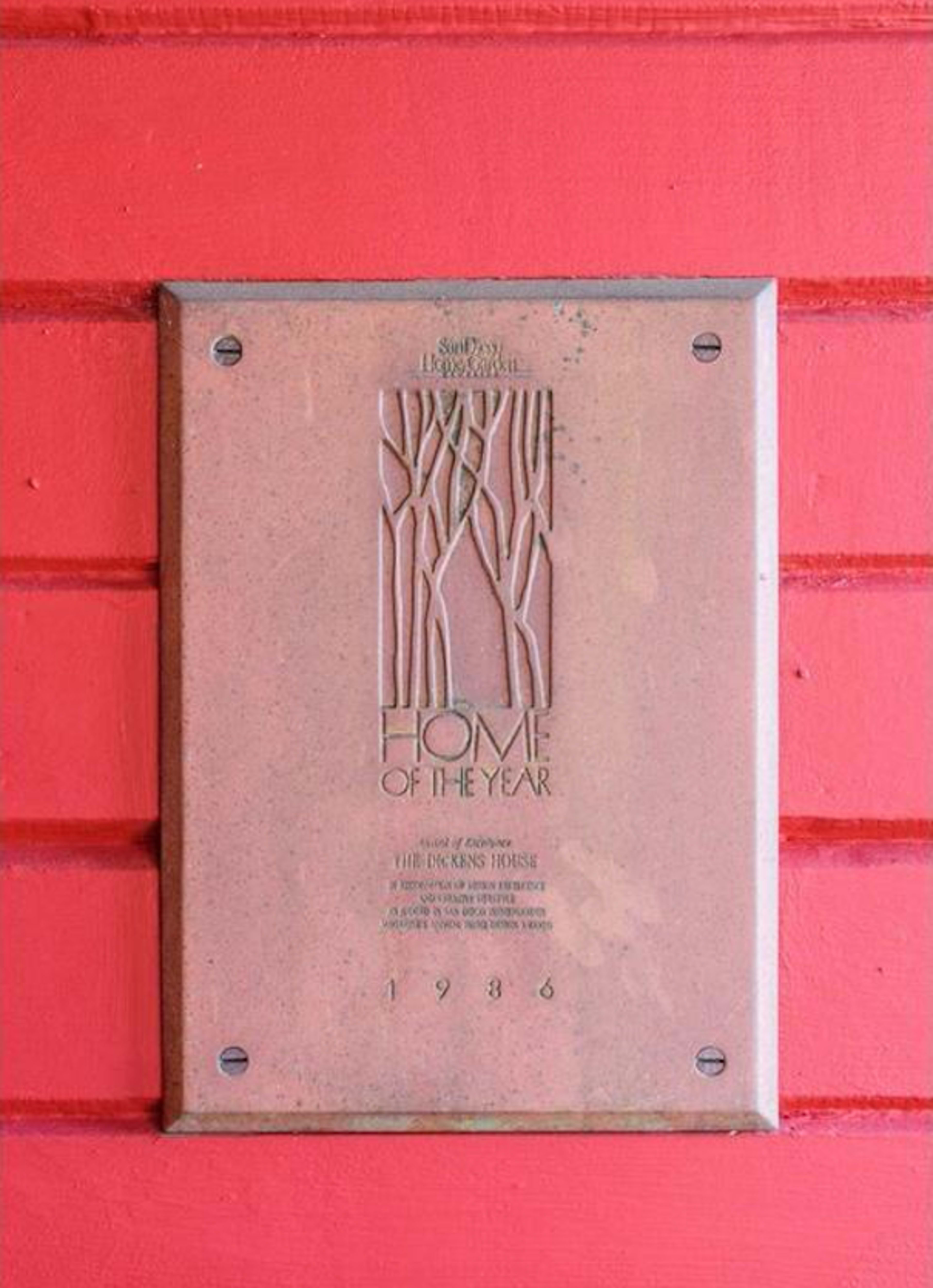 A bronze plaque titled "Home of the Year" is mounted on a red wooden wall.