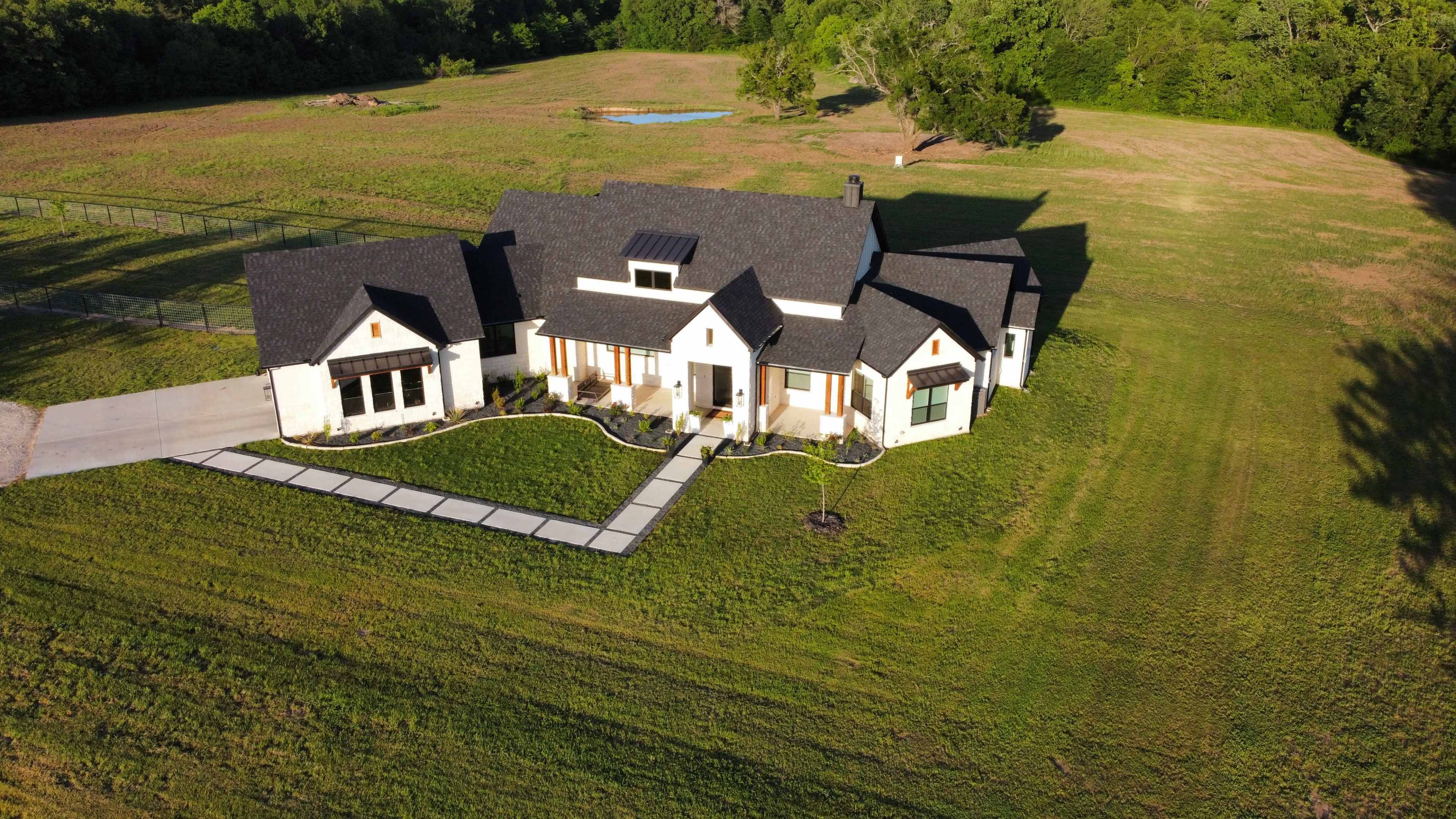 The image shows a modern, single-story house with a large lawn and a paved walkway leading to the entrance.