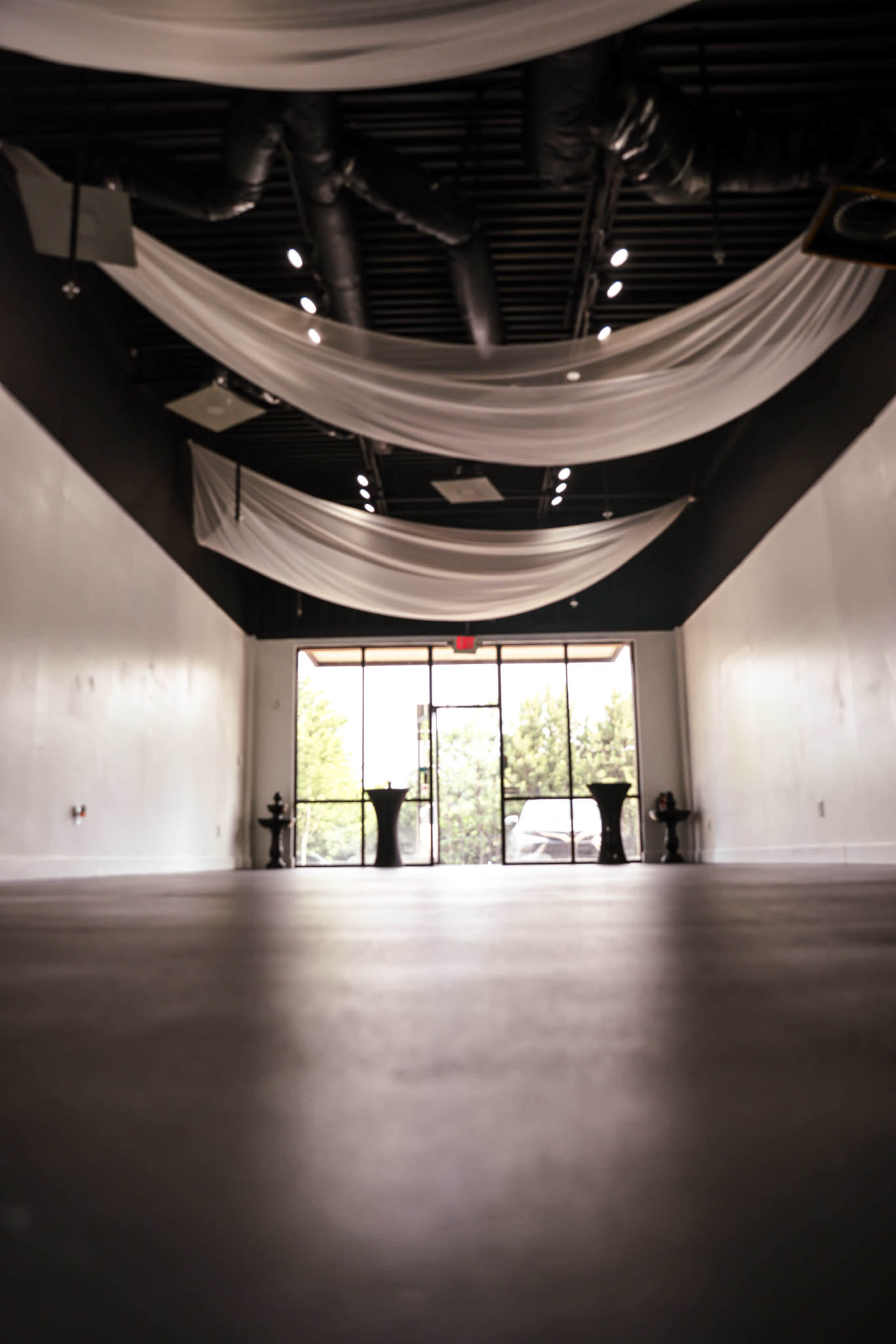 An empty, spacious interior with draped fabric overhead and two black tables near the entrance.