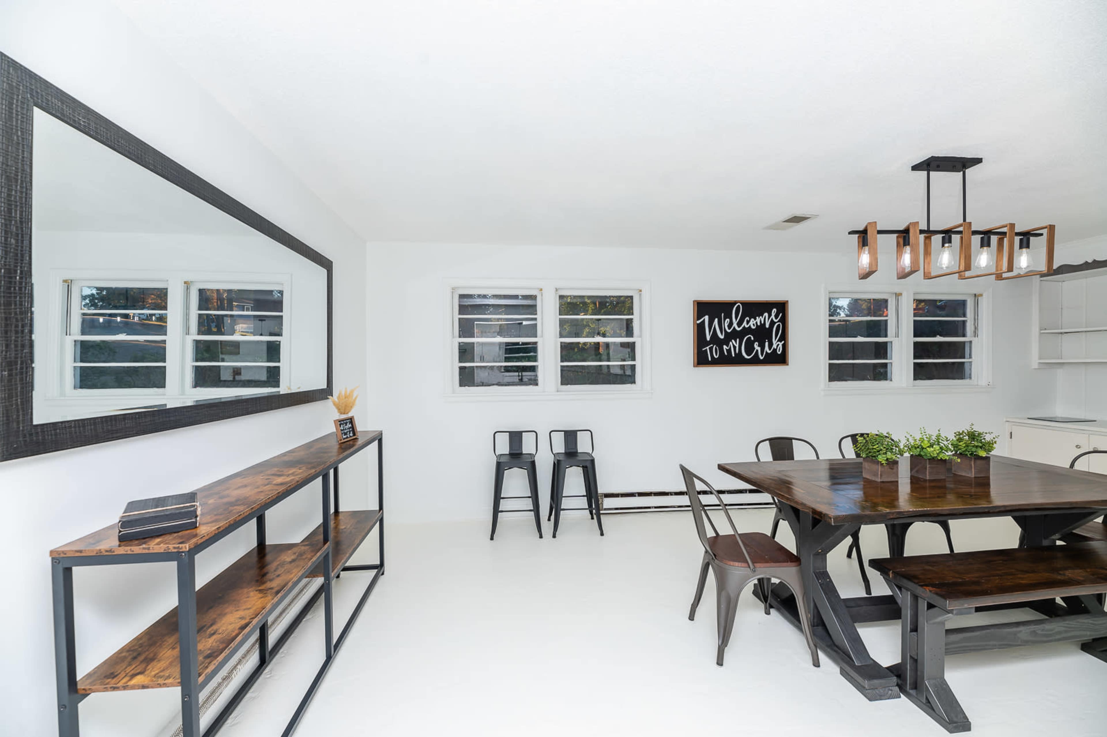 A bright dining area featuring a wooden table, black metal chairs, a console table against the wall, and framed wall art.